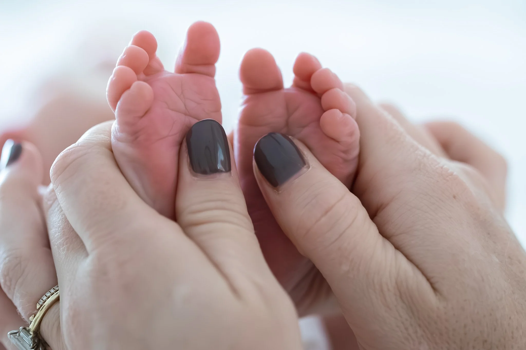 Close-up of a baby’s tiny hands being gently held by an adult with dark nail polish.