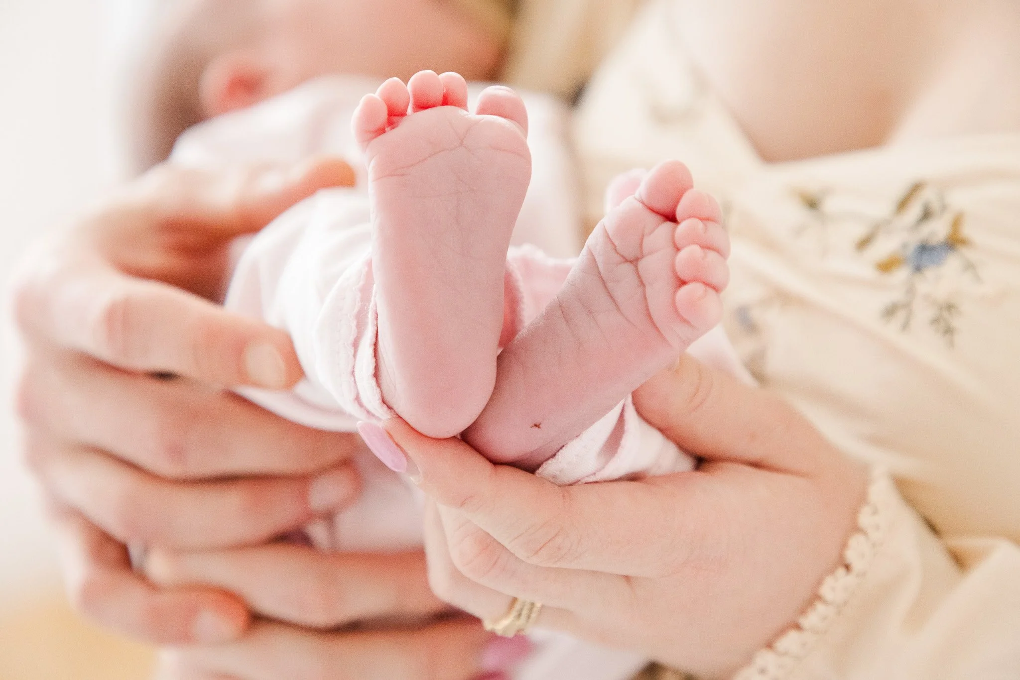 Close-up of a newborn baby's feet being gently held by an adult, with the baby lying on a patterned blanket.