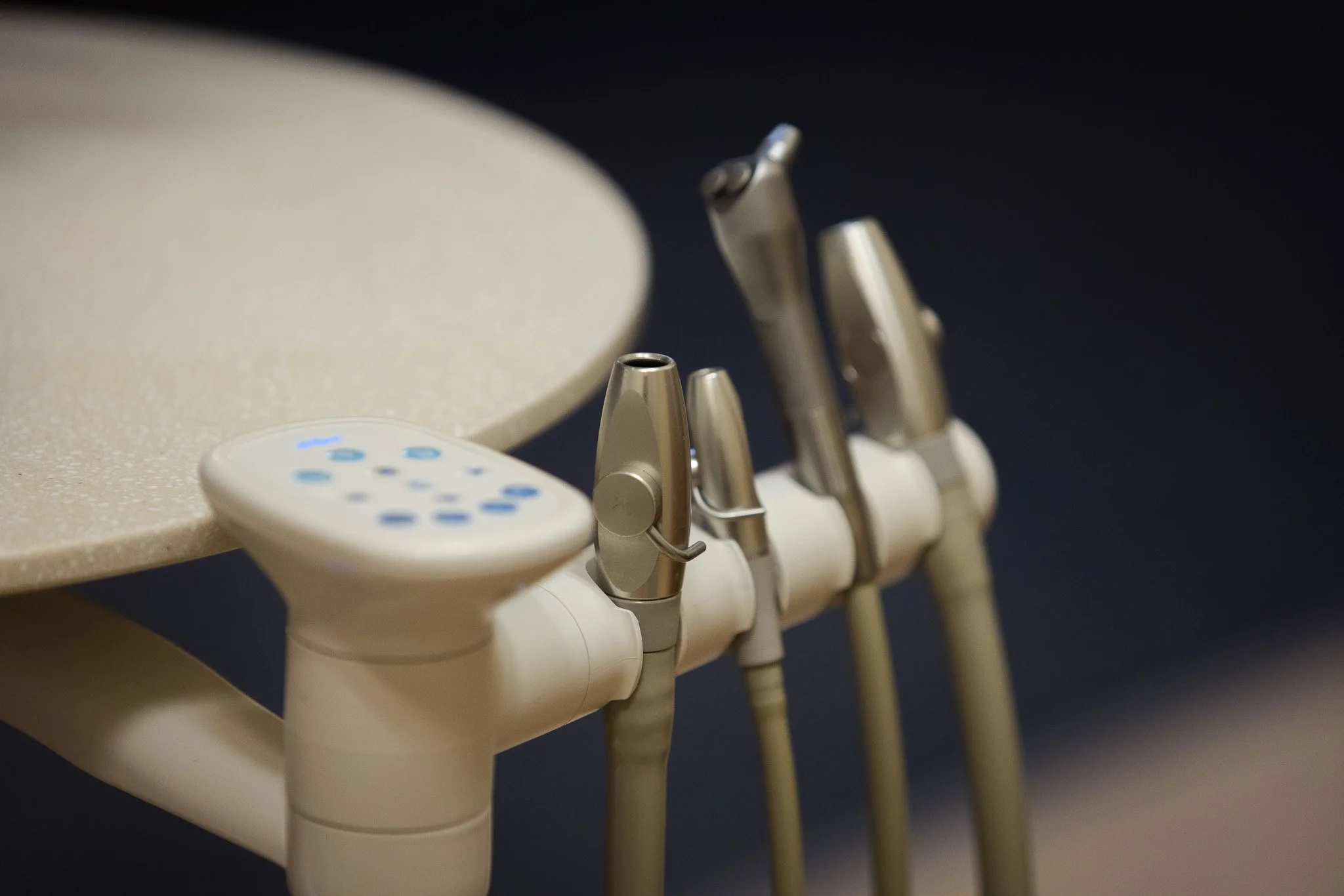 Close-up of a dental unit with three handpieces attached and a control panel, placed against a dark background.
