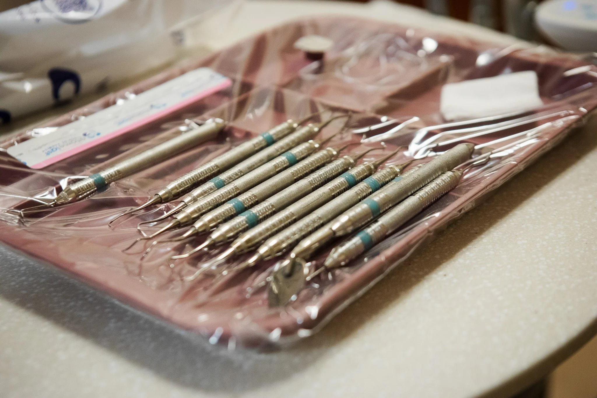 Set of dental hand tools on a tray, including dental picks and mirrors, covered with a plastic sheet.