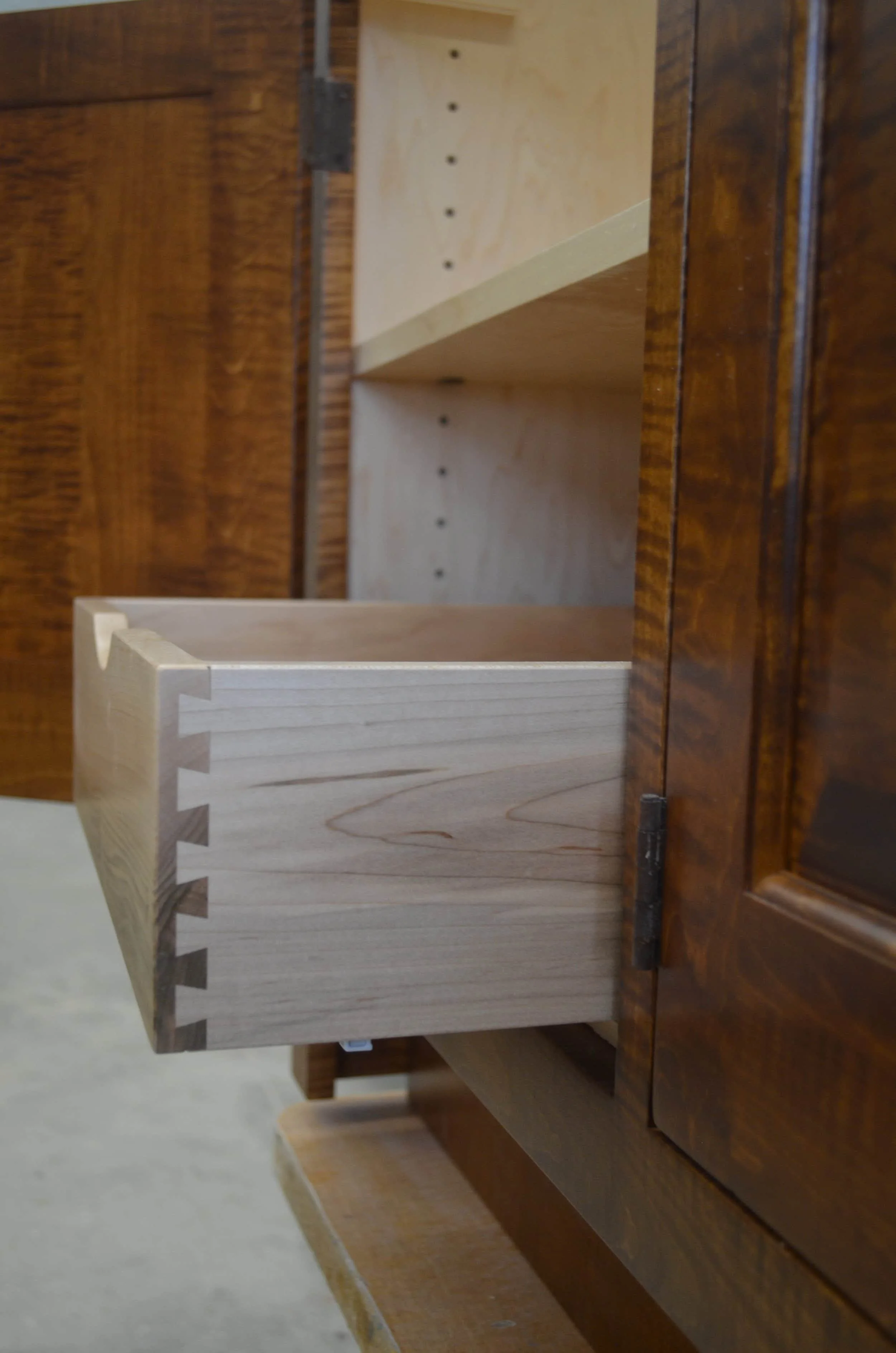 Custom curly maple cabinet with hand-cut dovetail drawer joints showing premium hardwood grain and traditional joinery