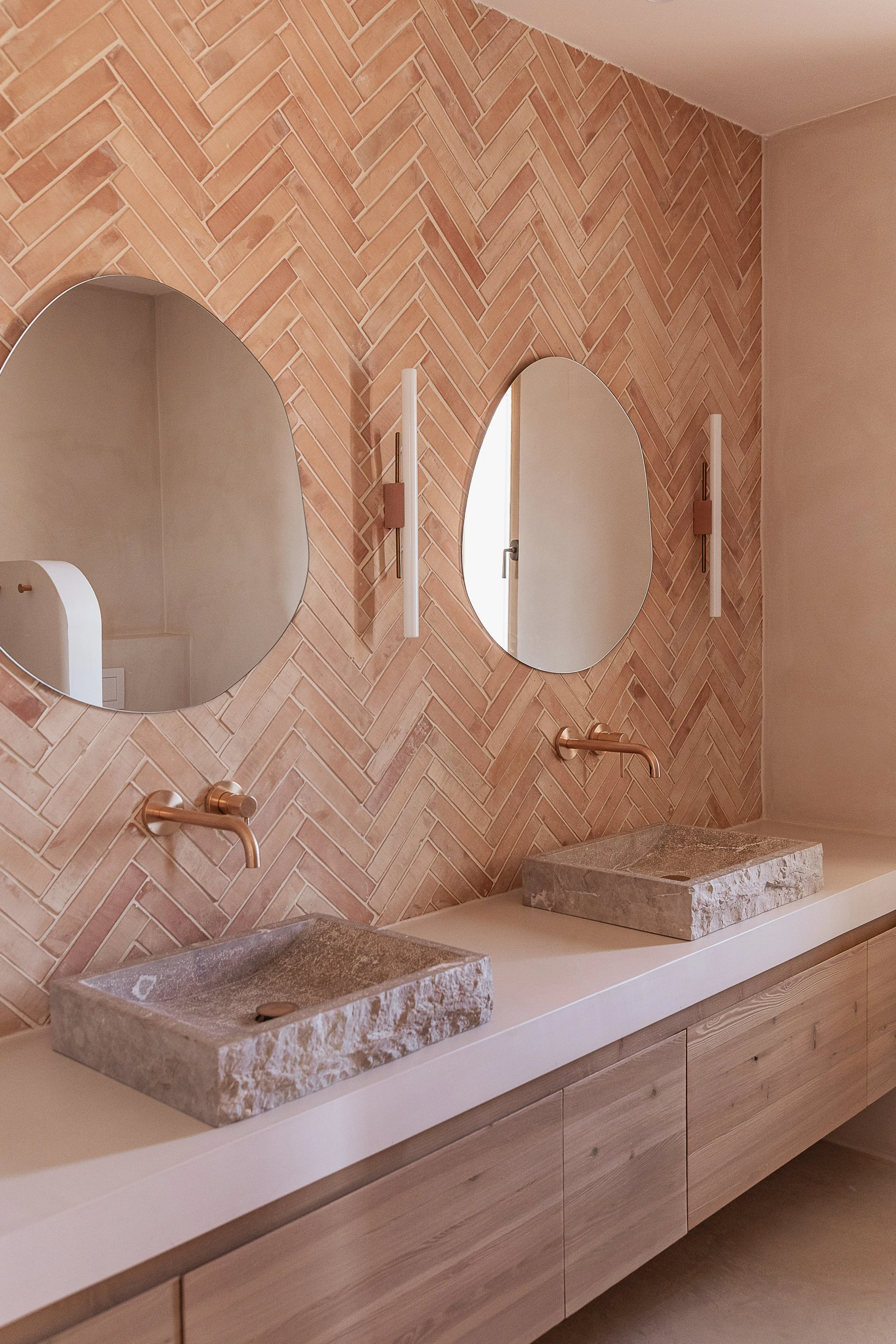 Bathroom with handmade terracotta herringbone wall tiles, reclaimed stone basins and custom oak vanity in a Mediterranean home in Mallorca.