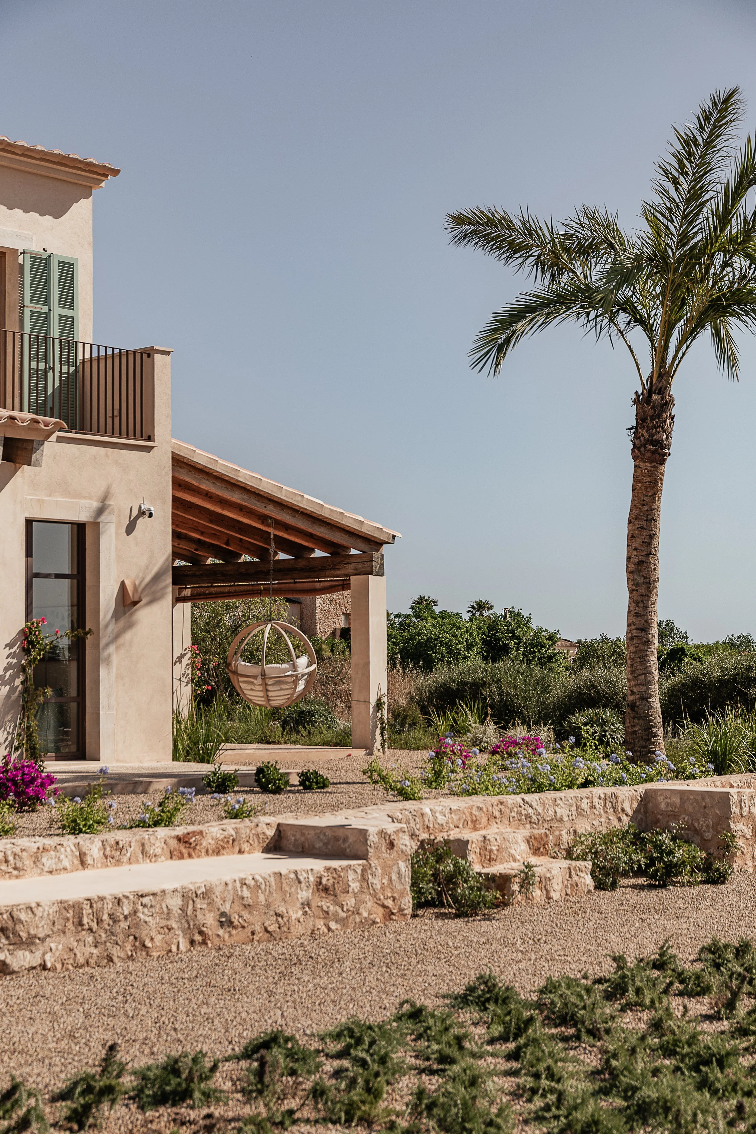 Exterior of a Mediterranean family home with shaded terrace, native landscaping and traditional Mallorcan architecture designed for outdoor living.
