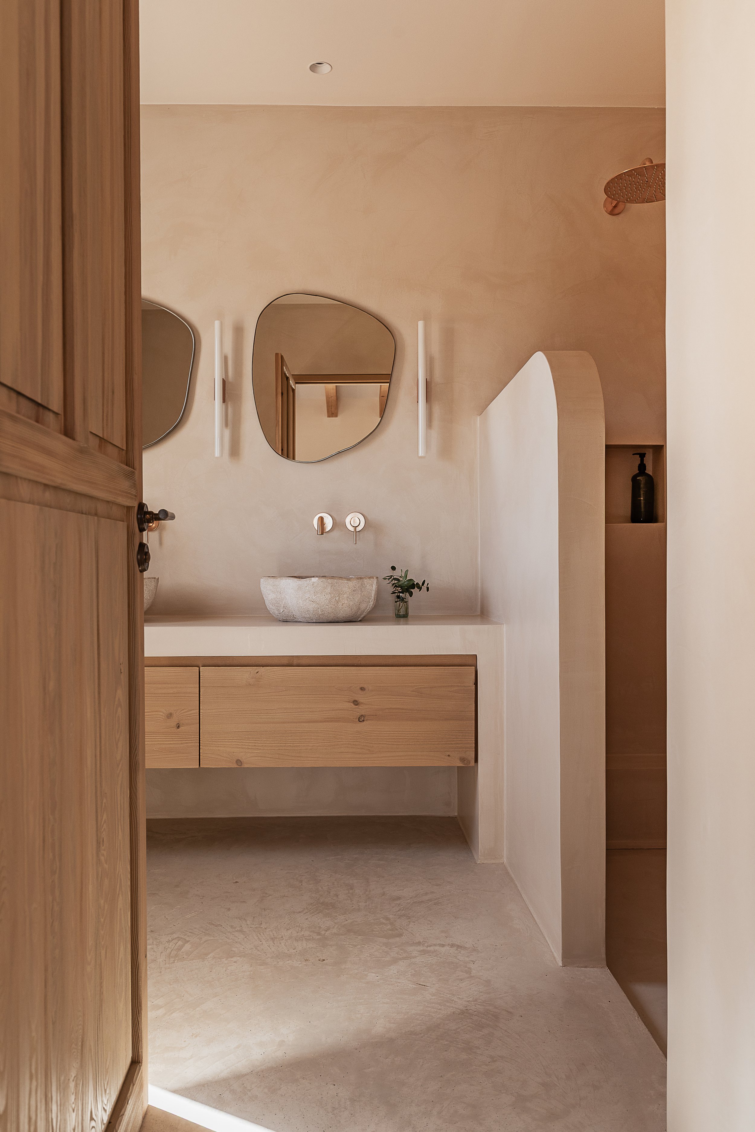 View into a Mediterranean bathroom with seamless microcement, custom oak vanity and reclaimed stone basin in a Mallorca family home.