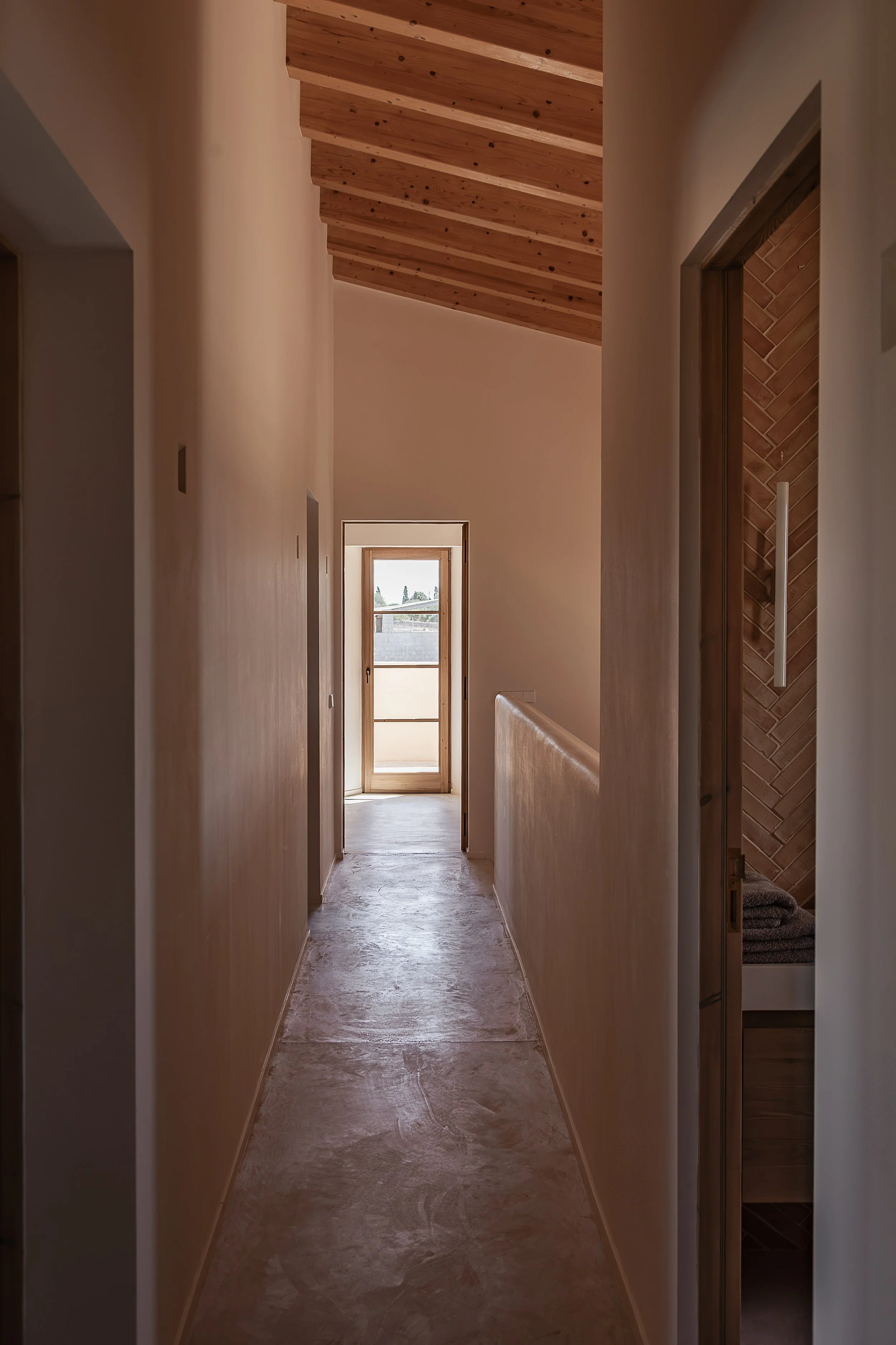 Hallway with seamless microcement flooring, lime-plastered walls and exposed timber ceiling in a Mediterranean home in Mallorca.