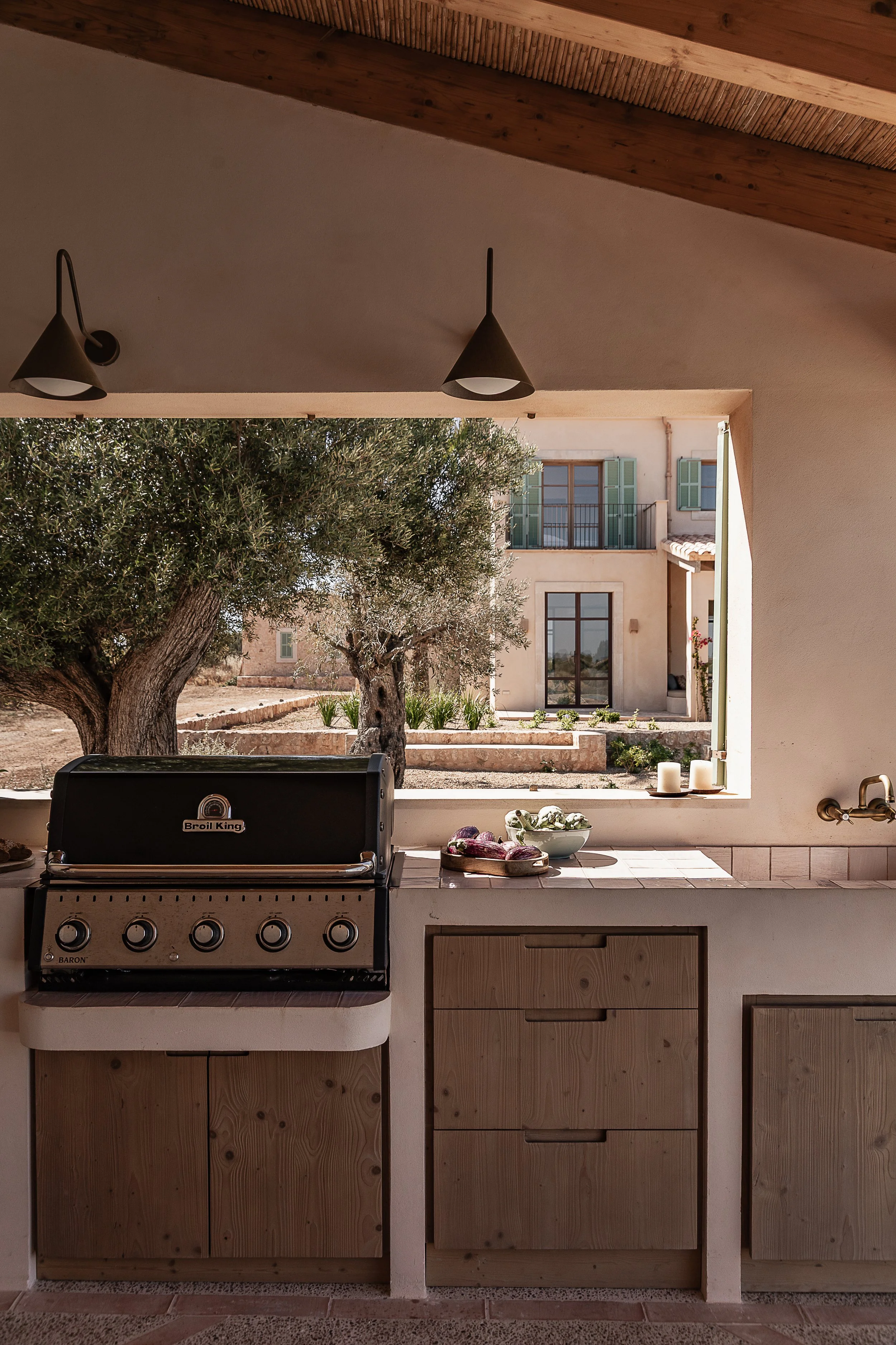 Outdoor kitchen with custom oak cabinetry, handmade terracotta flooring and framed views across a Mediterranean home in Mallorca.