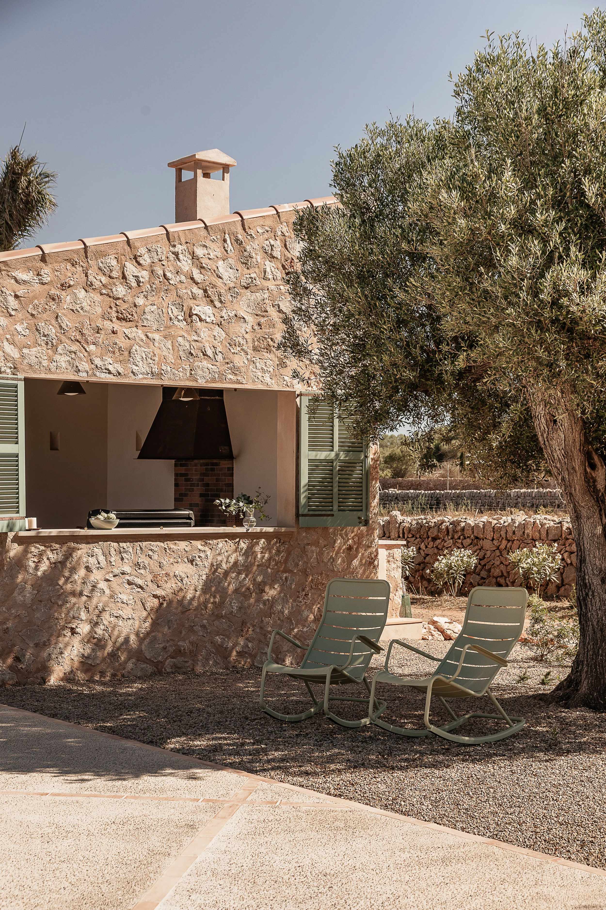 Covered outdoor kitchen and shaded seating beneath an olive tree, designed for Mediterranean outdoor living in Mallorca.