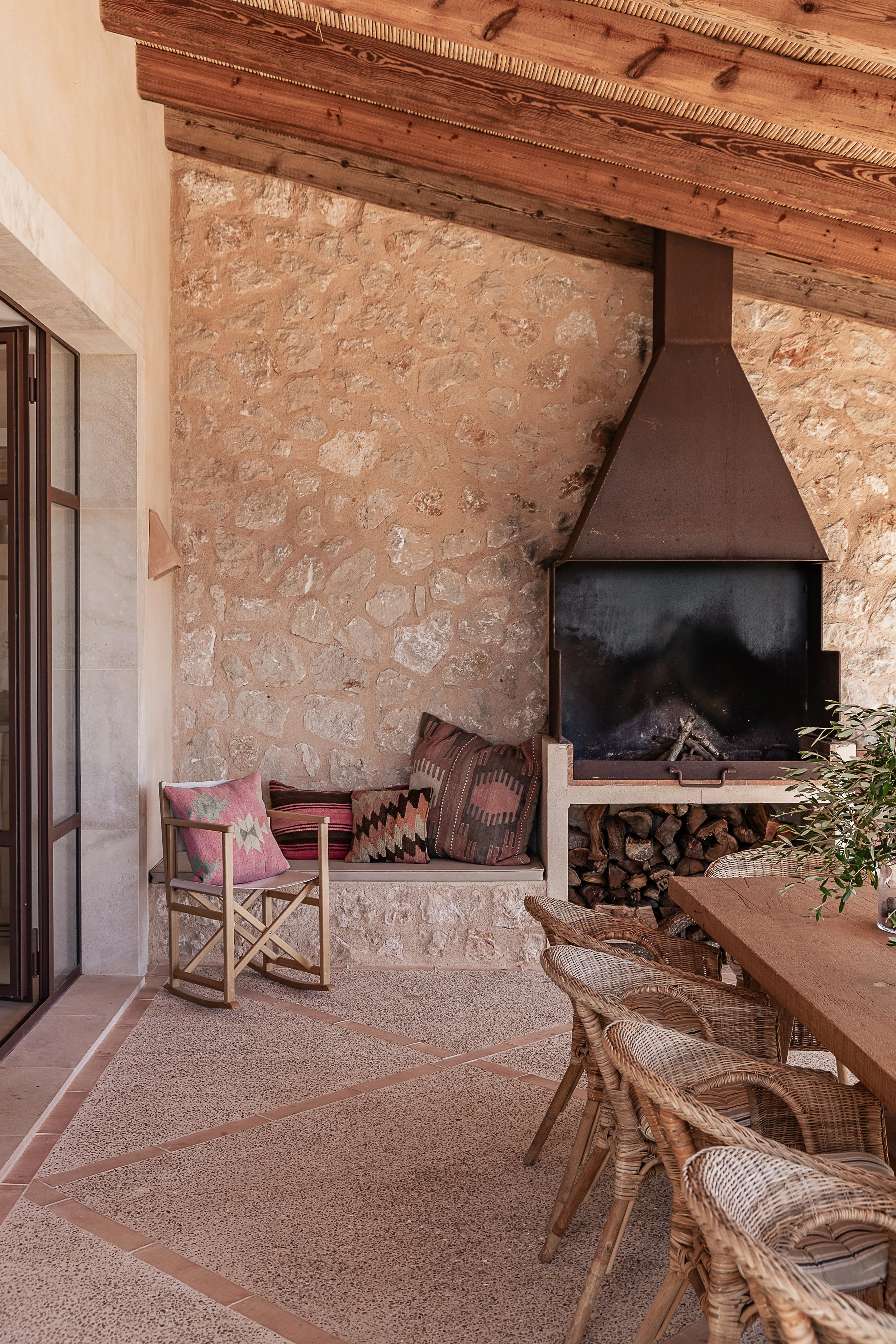 Covered terrace with natural stone walls, outdoor fireplace and handmade terracotta flooring in a Mediterranean home in Mallorca.