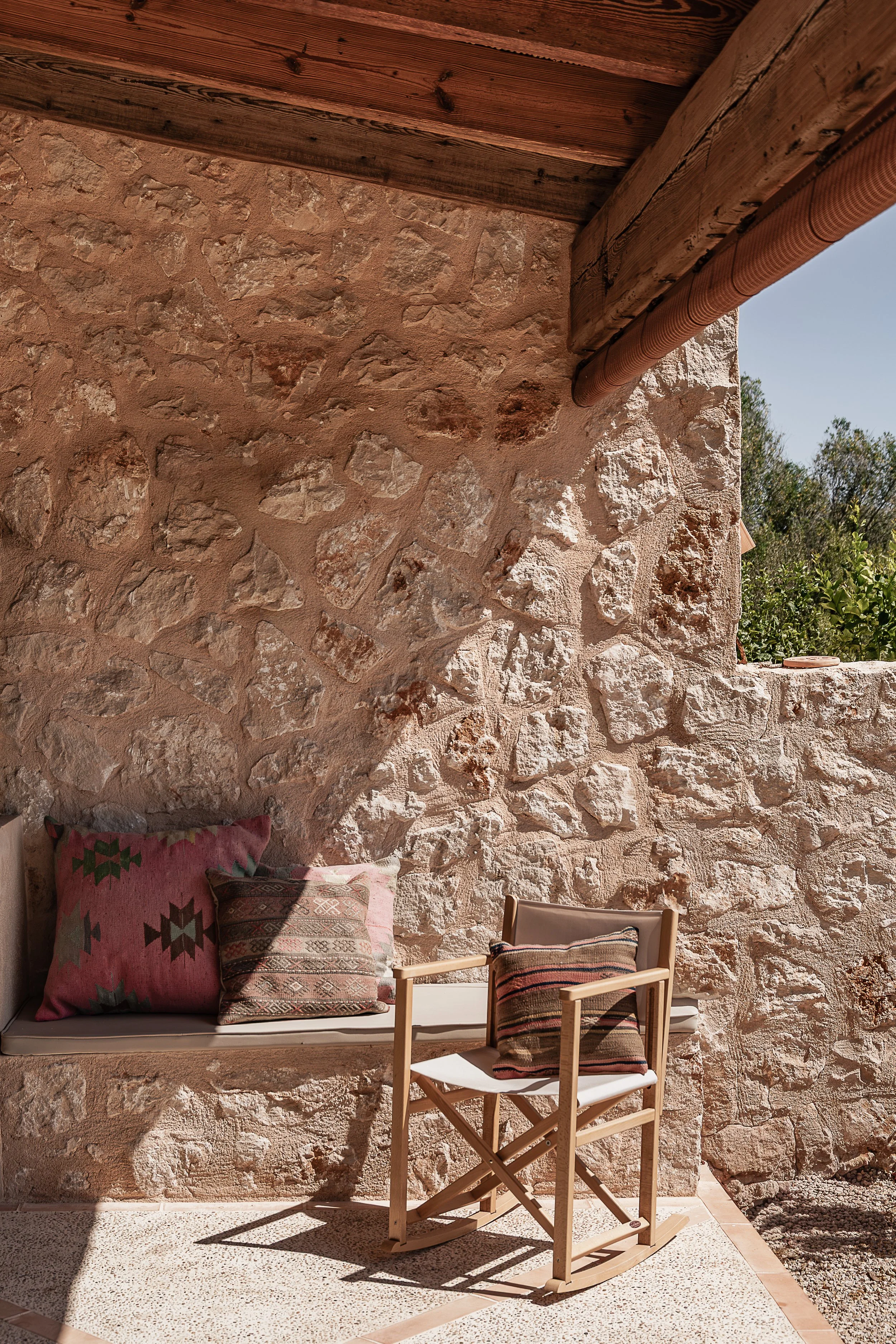 Covered terrace with natural stone walls, exposed timber beams and built-in seating in a Mediterranean home in Mallorca.
