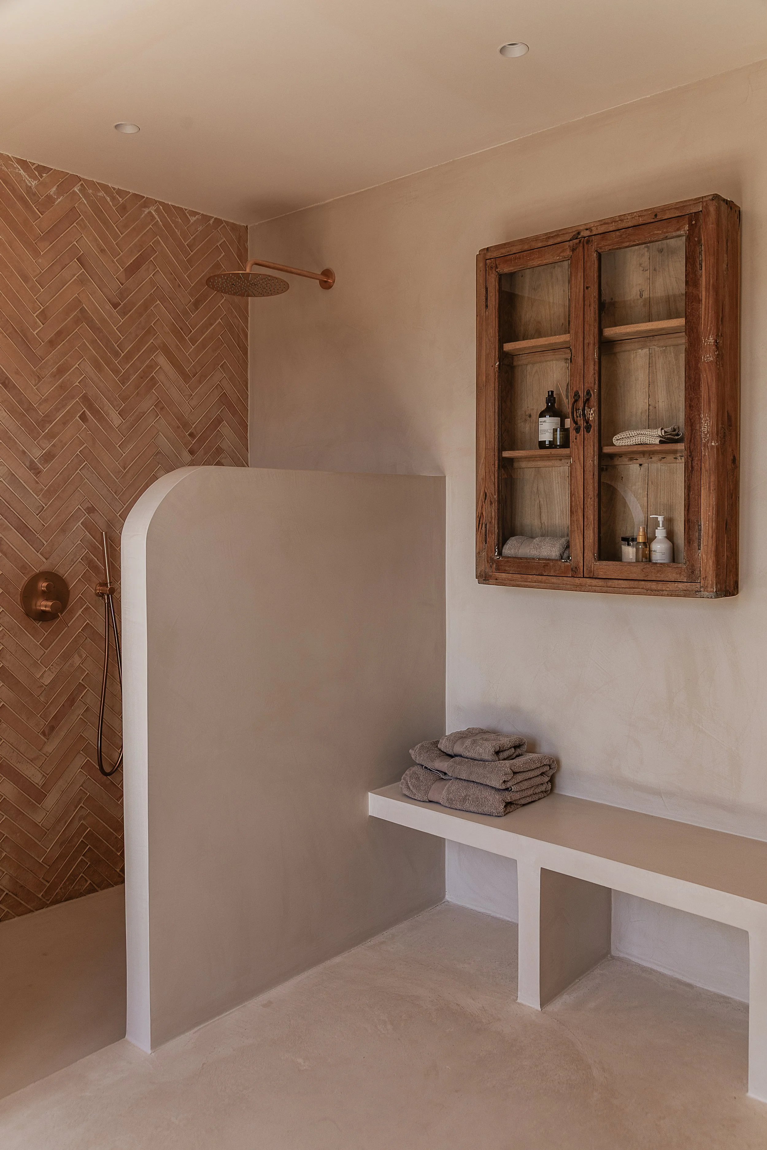 Bathroom with handmade terracotta herringbone tiles, seamless microcement surfaces and a reclaimed vintage cabinet in a Mediterranean home in Mallorca.