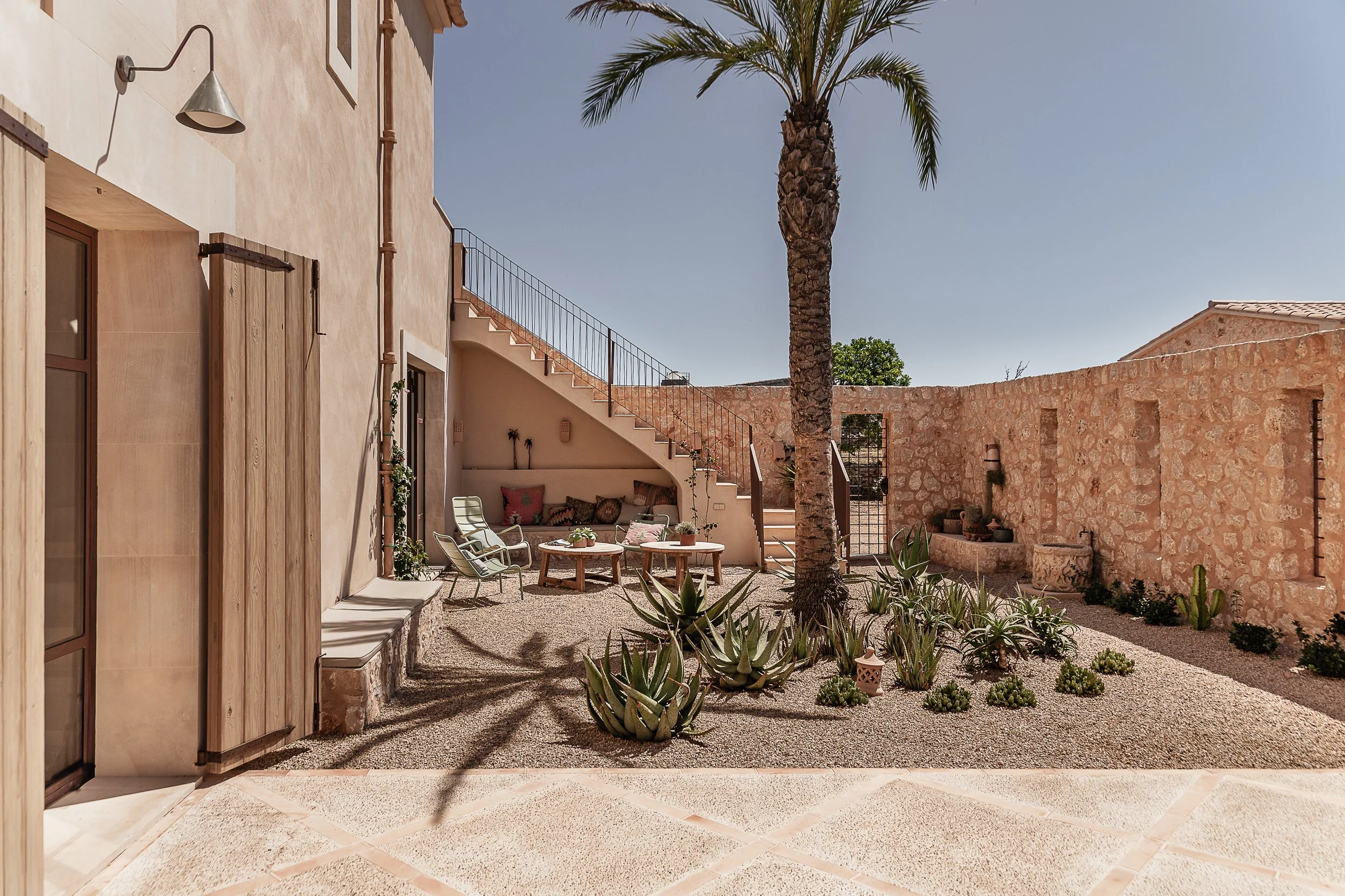 Mediterranean courtyard in Mallorca with shaded outdoor seating, natural stone walls and traditional exterior staircase designed by espanyolet.