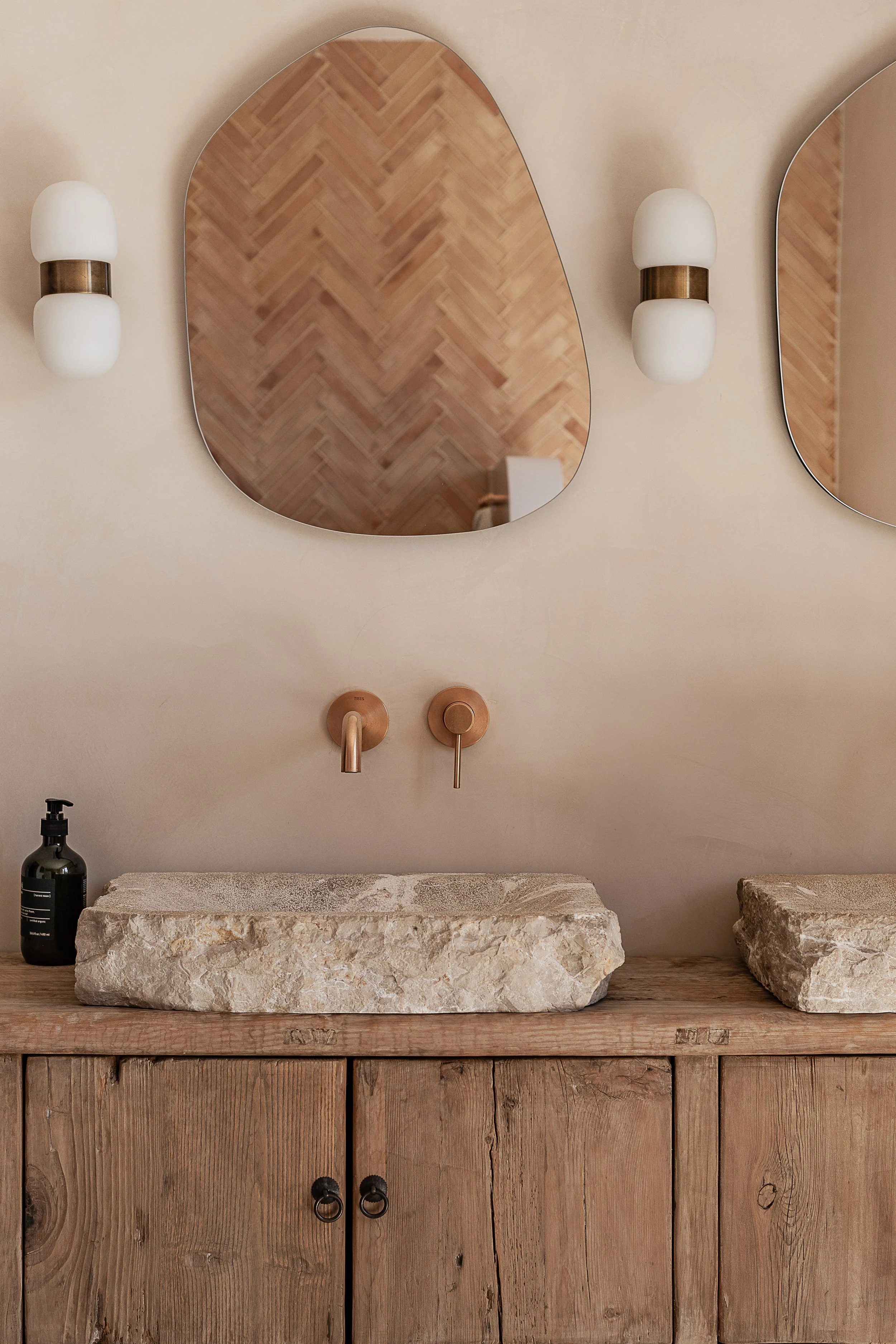Bathroom with reclaimed stone basins, rustic oak vanity, lime-plastered walls and handmade terracotta tiles in a Mediterranean home in Mallorca.