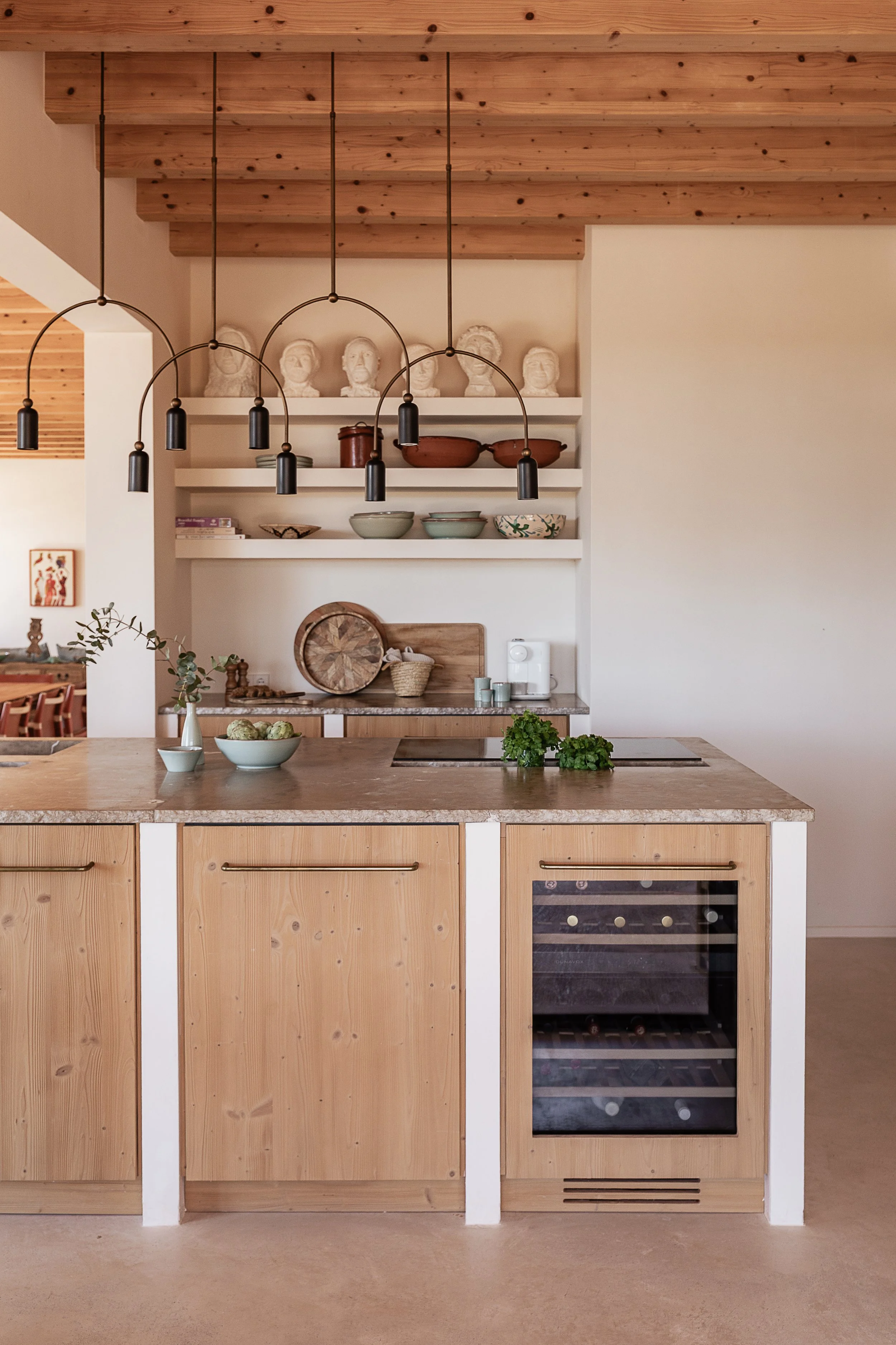 Kitchen with custom oak cabinetry, natural stone worktops, open shelving and exposed timber beams in a Mediterranean home in Mallorca.