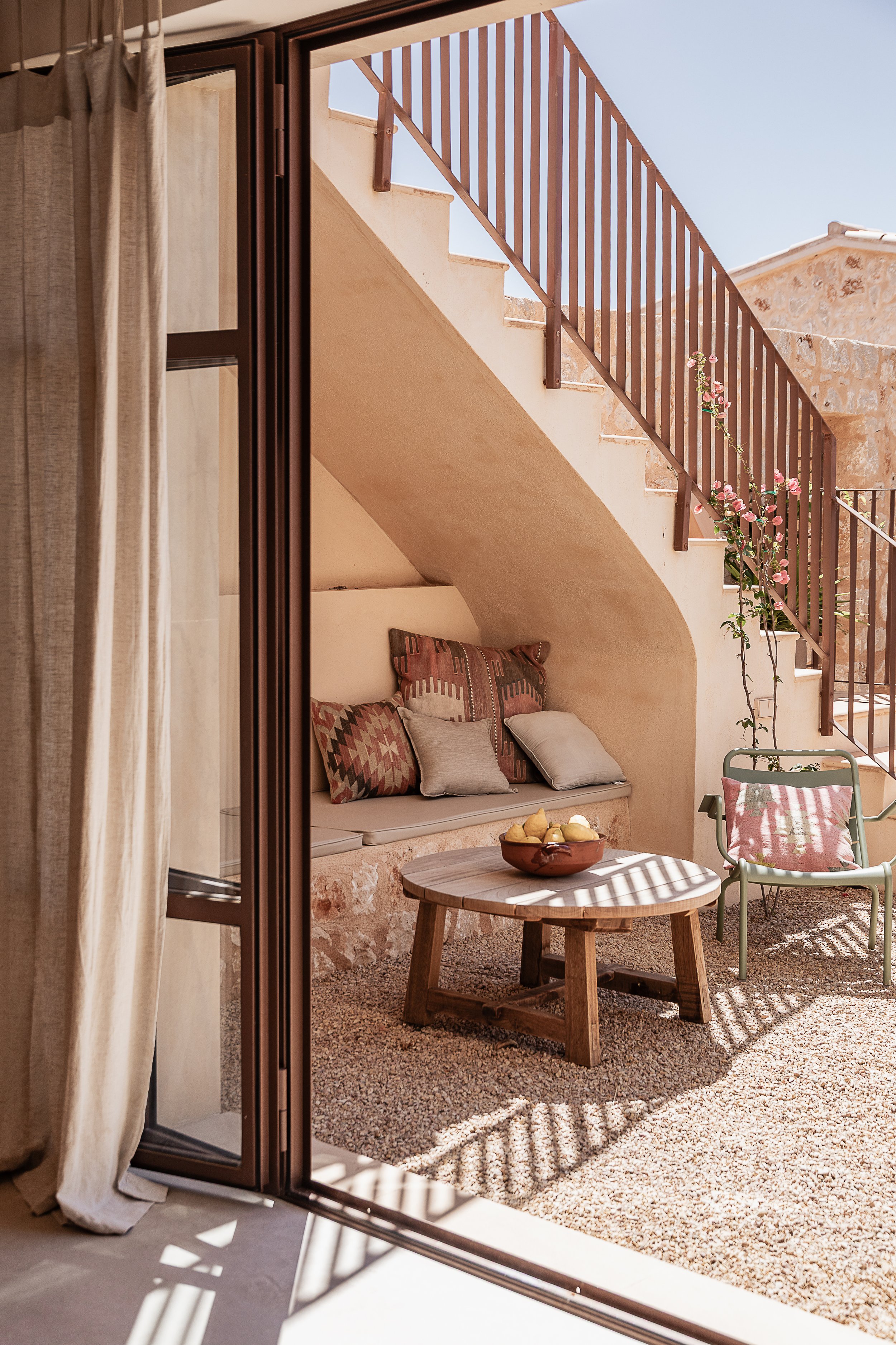 Indoor-outdoor living in a Mediterranean home in Mallorca, with oak-framed doors opening onto a shaded courtyard and stone staircase designed by espanyolet.
