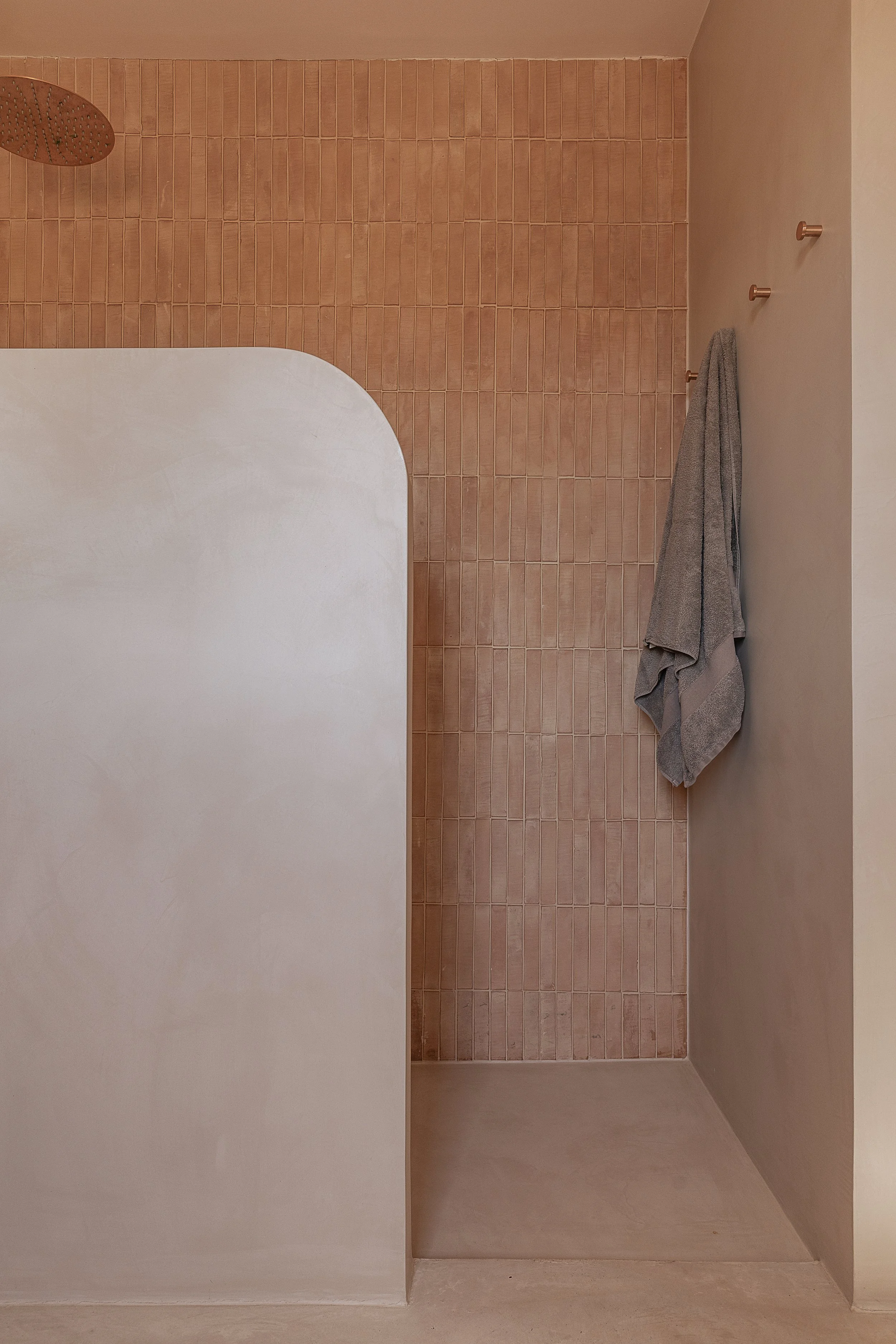 Walk-in shower with handmade terracotta wall tiles, curved plaster partition and seamless microcement floor in a Mediterranean home in Mallorca.