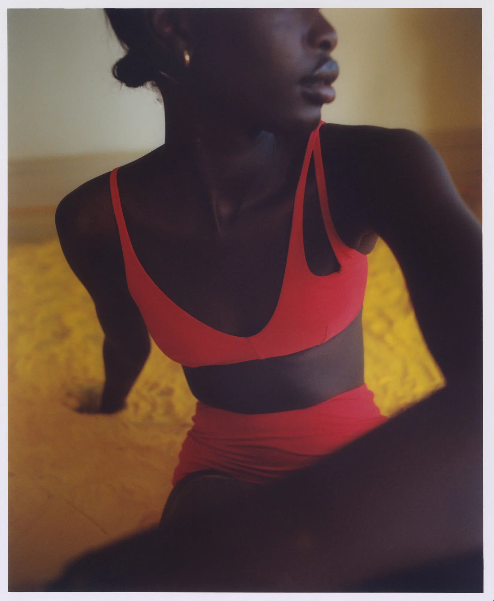 Close-up of a woman in athletic wear, with focus on her shoulder, arm, and part of her face, standing on a yellow surface.