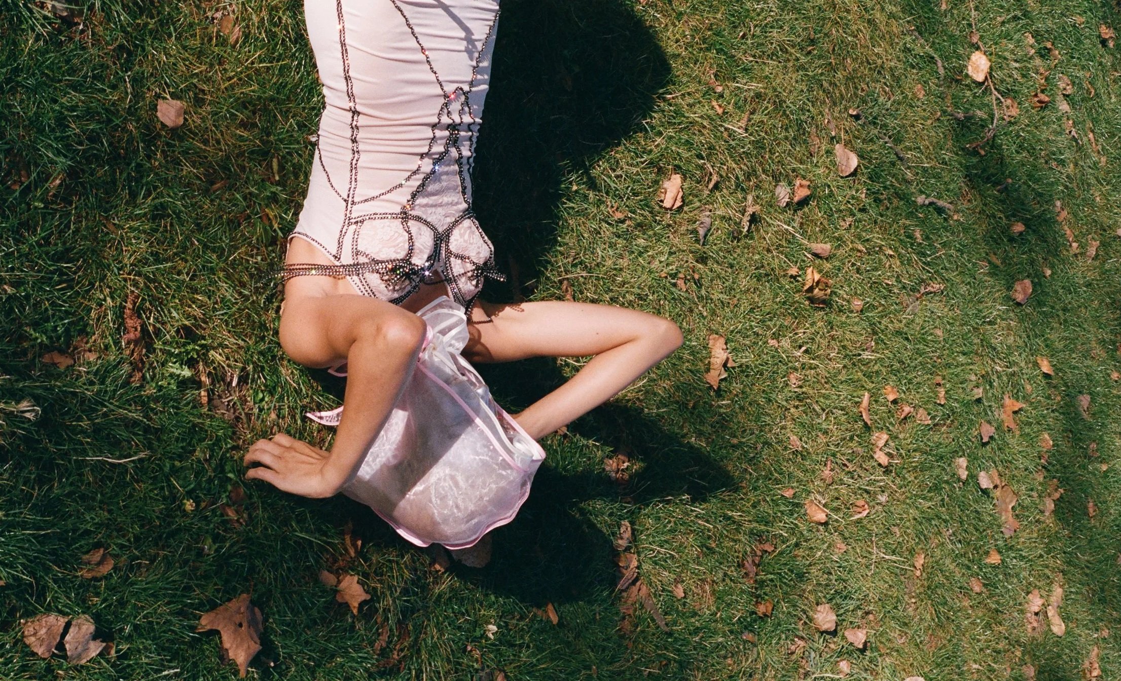 A woman lying on the grass on a sunny day, wearing a white and black top with chain details, a pink tutu-style skirt, and a pink handbag nearby.