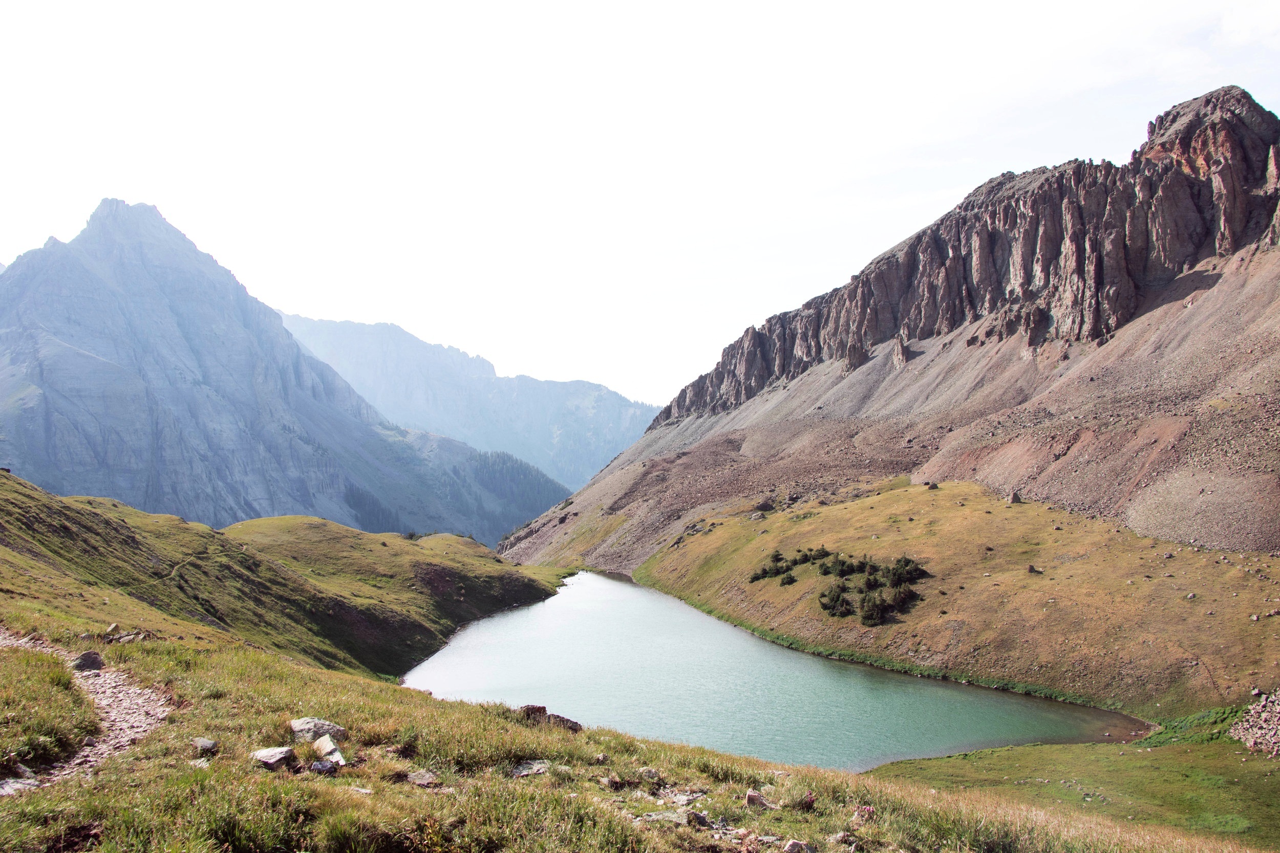 Mountainous landscape with a small lake, grassy hills, and rocky cliffs.