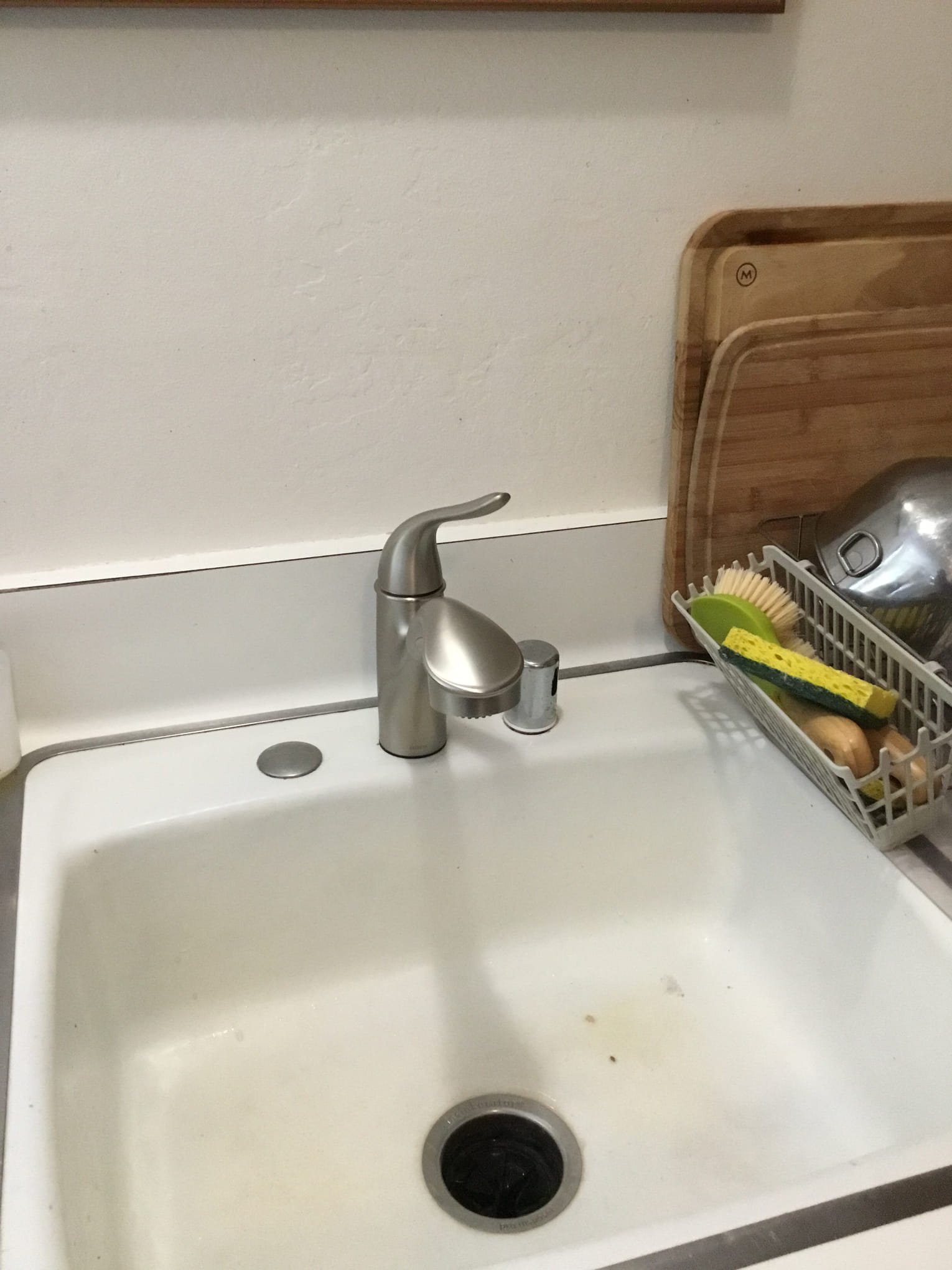 Kitchen sink with a silver faucet, a wooden cutting board, and a dish rack with cleaning sponges and a scrub brush.