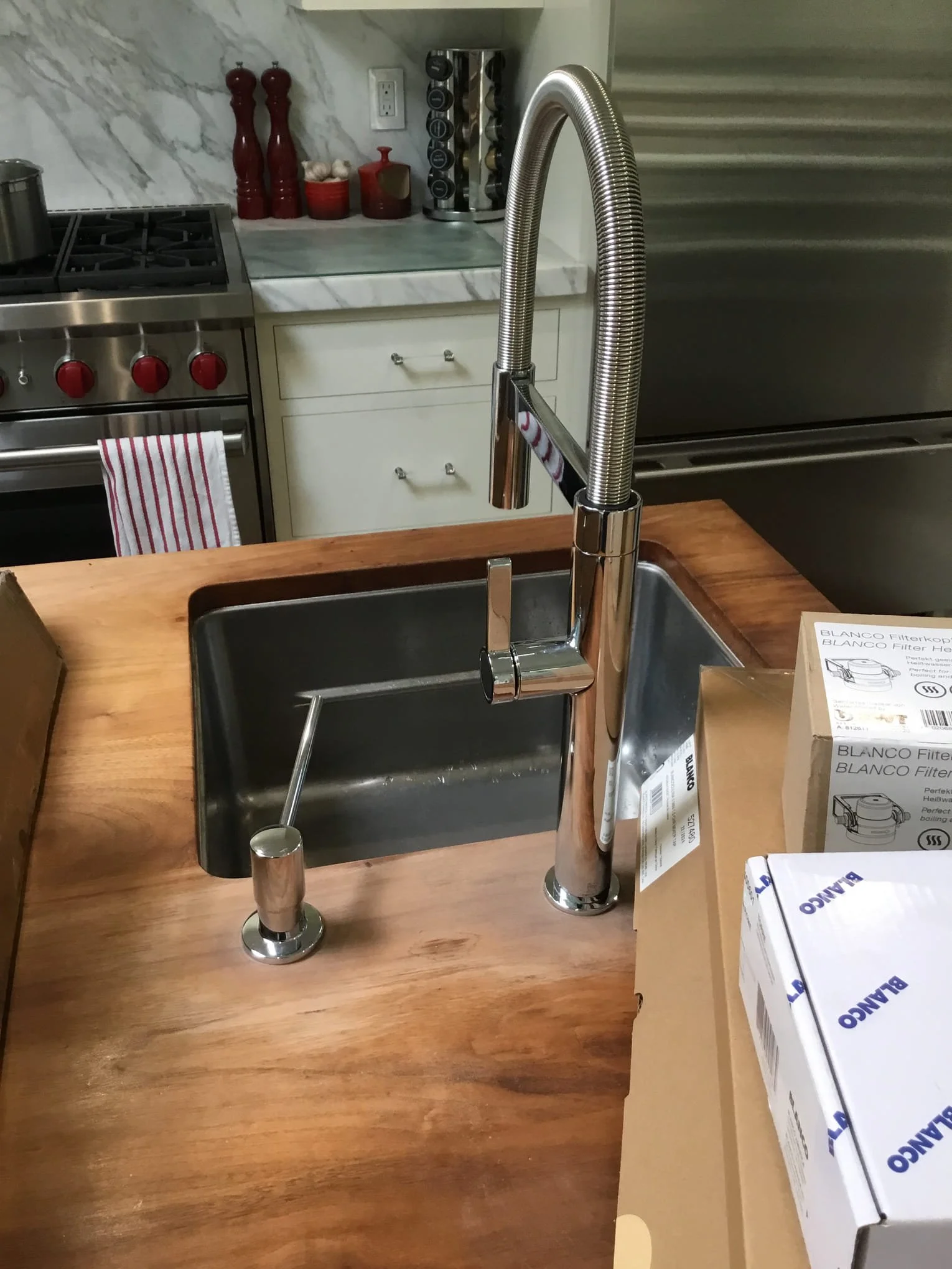 Kitchen sink with a chrome faucet, a black sink basin, and packaging boxes on a wooden countertop.