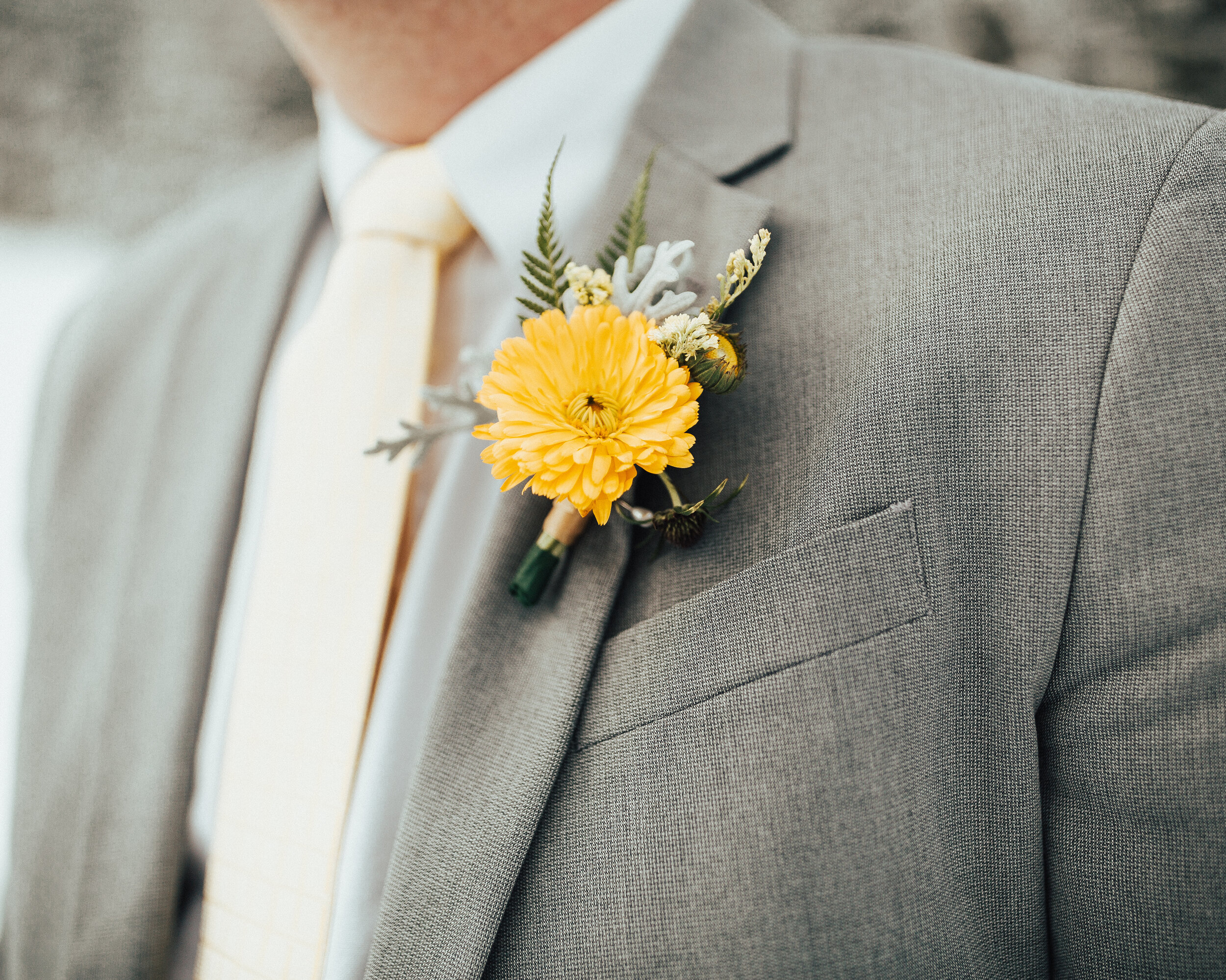  A yellow and frosted greenery boutonniere crafted by Cache Valley, Utah’s Sweet Afton Floral adds the perfect pop of color this groom’s gray suit needs. gray mens wedding suit, mens wedding boutonniere, yellow dainty wedding boutonniere, peach color