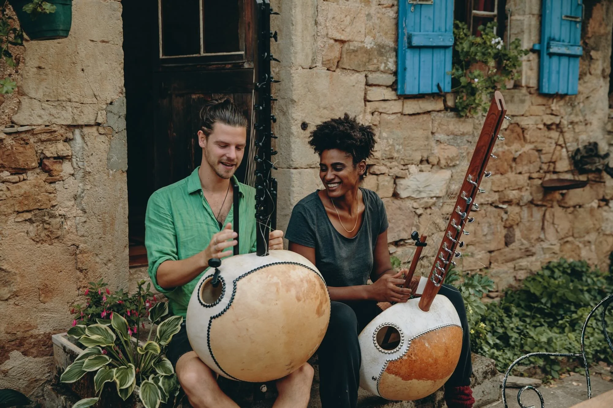 Josh Doughty teaching at a kora workshop in France, guiding students as they play traditional West African harps (koras) in front of a rustic stone building with blue shutters.