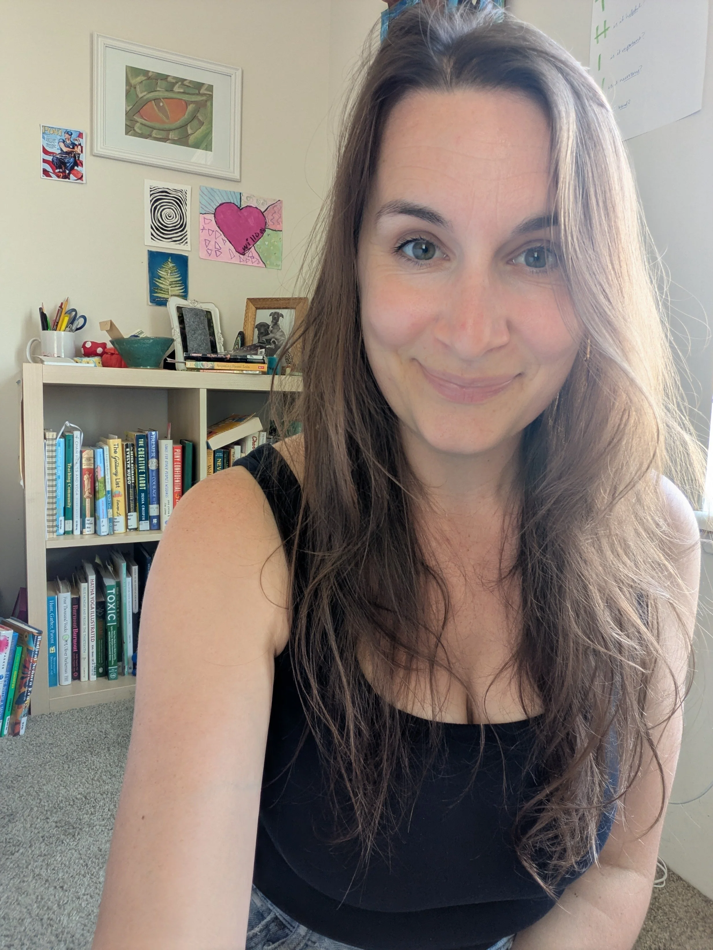 profile image of the author (Alycia Buenger) with a messy bookshelf and a wall of art in the background