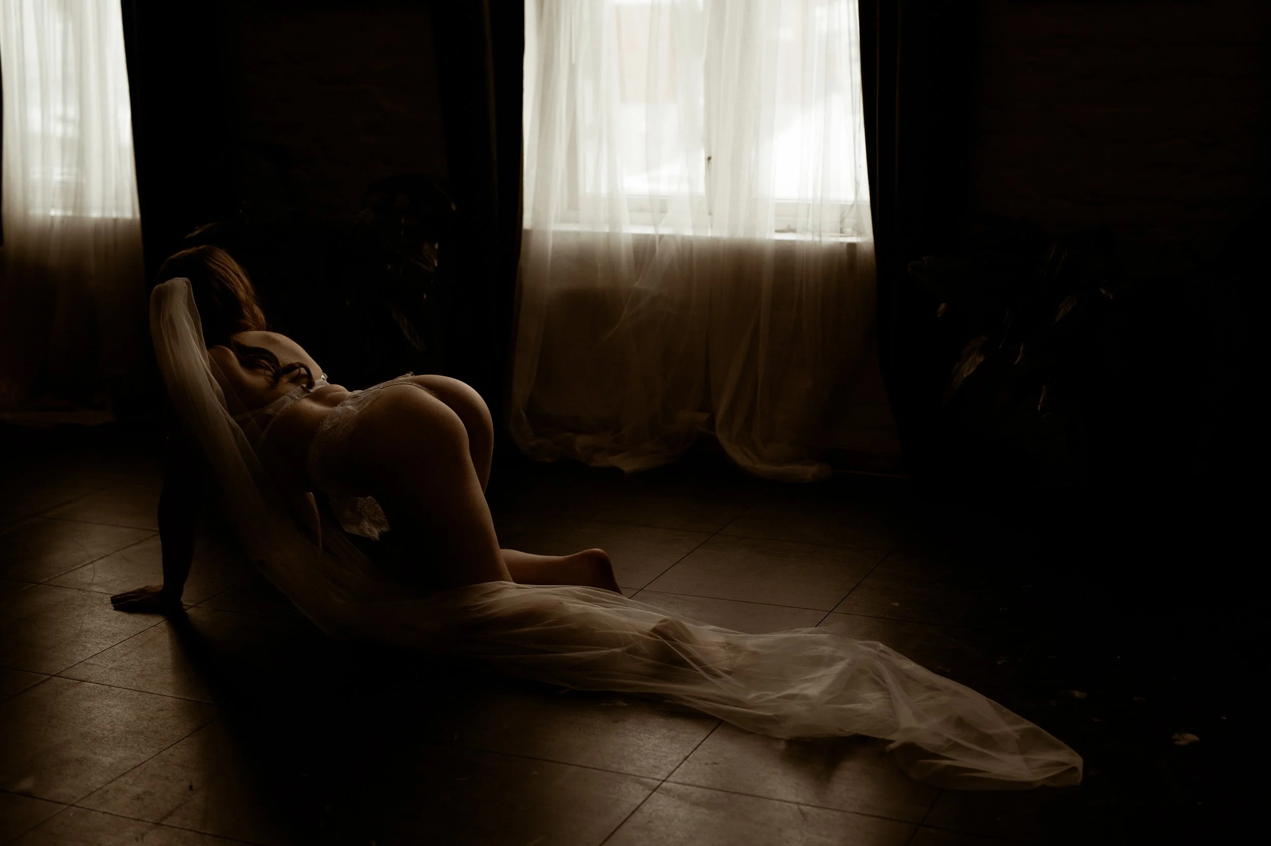 En dame med brudeslør og undertøy som sitter foran et vindu