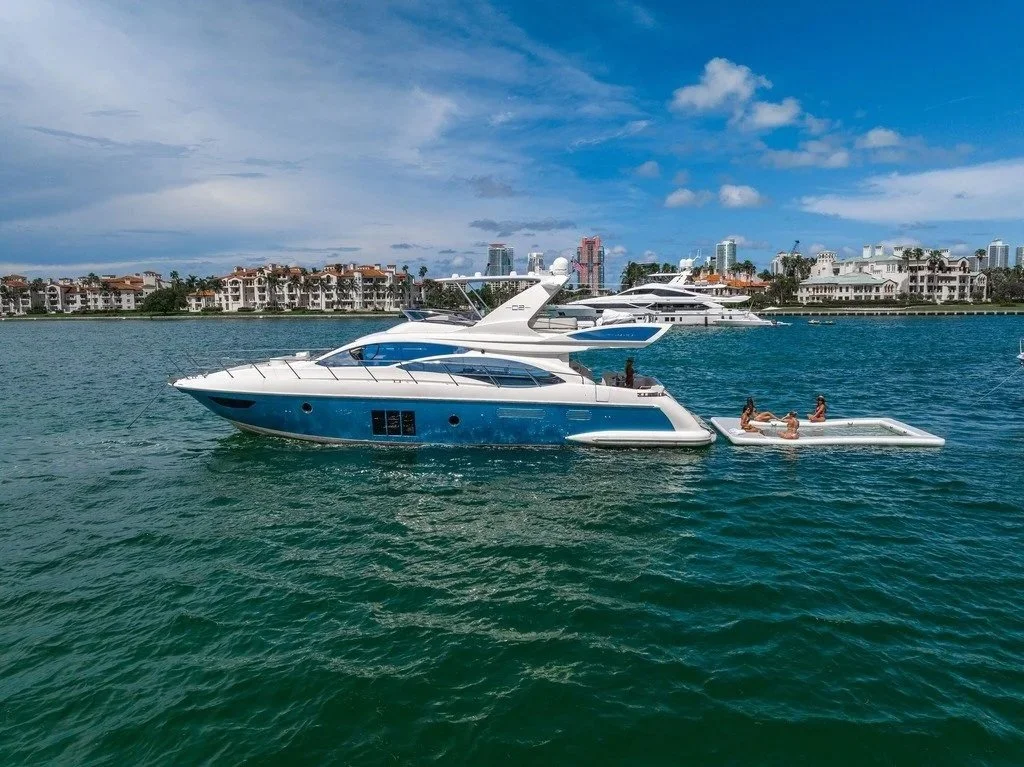 Luxury yachts anchored in a bay with a city skyline and partly cloudy sky in the background.