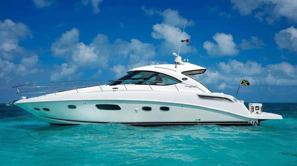 A white motor yacht cruising on blue ocean waters under a partly cloudy sky, with flags on it.