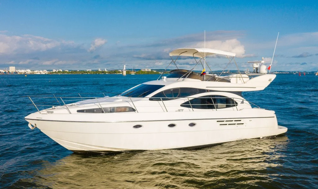 A white yacht sailing on blue water with a city skyline and partly cloudy sky in the background.