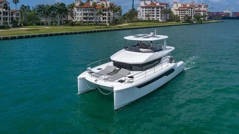 Luxury white yacht cruising through turquoise water near a city waterfront with high-rise buildings and palm trees.