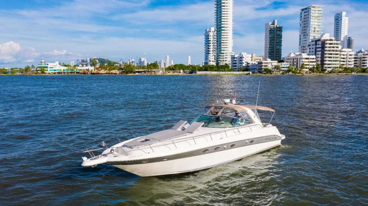 A white yacht sailing on a body of water with a city skyline and tall buildings in the background under a blue sky with clouds.
