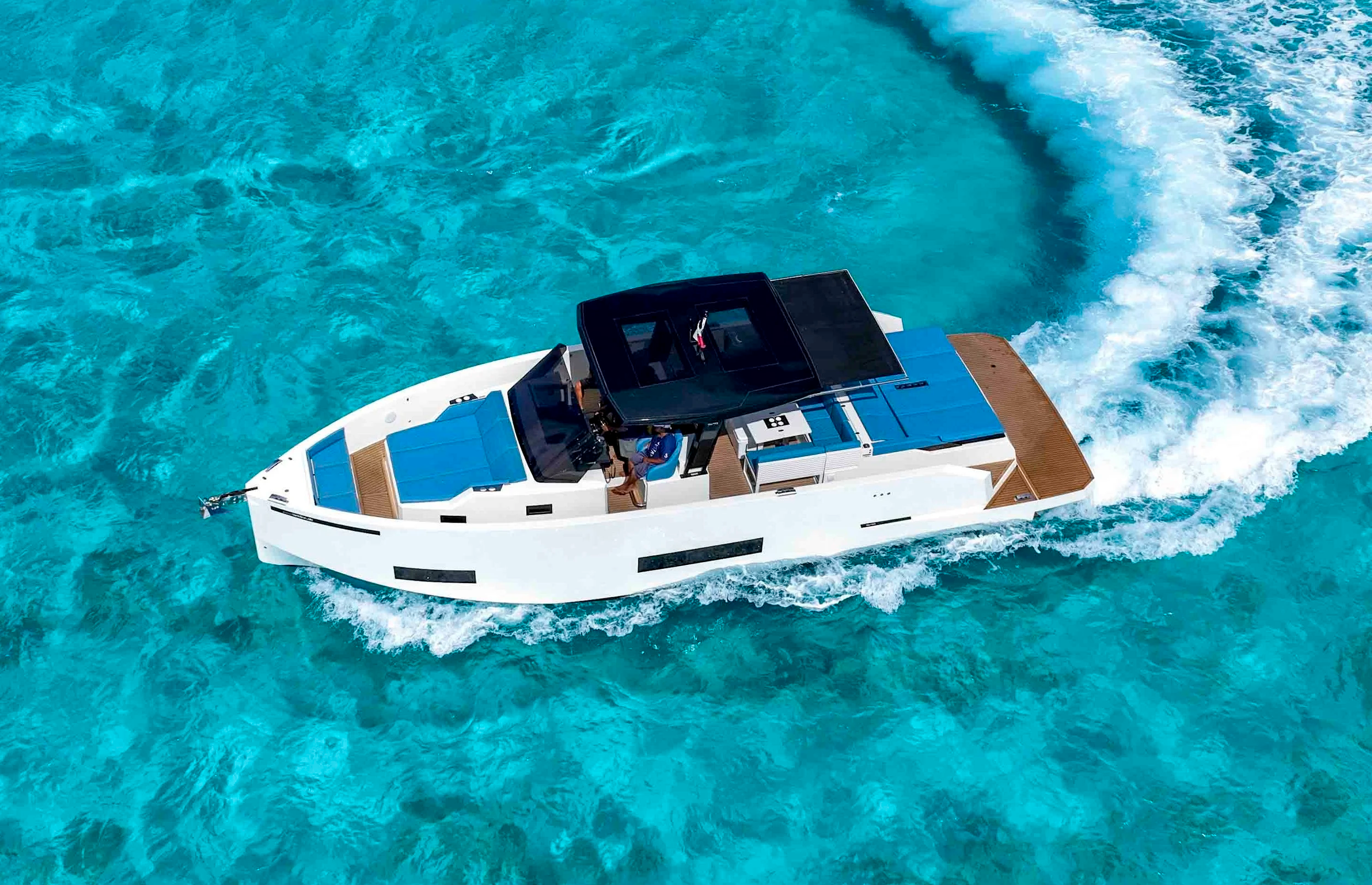 A white yacht with a black roof navigating through clear blue ocean waters, creating a wake behind it.
