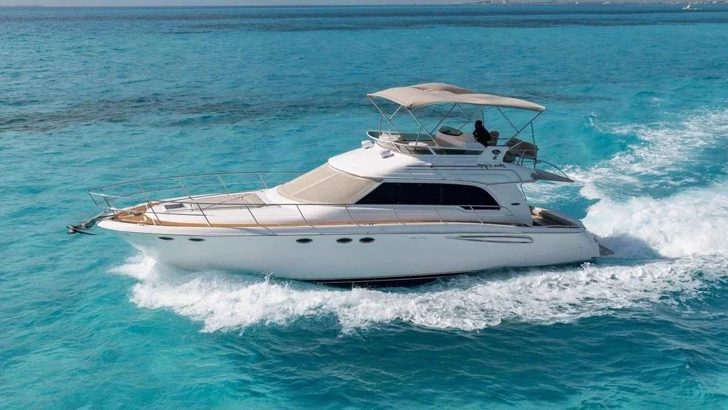 A white yacht moving through turquoise ocean water with a person on the upper deck.