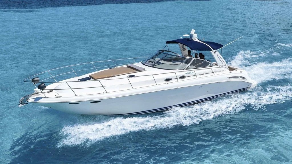 A white motor yacht speeding through blue water with a black canopy and two people aboard.