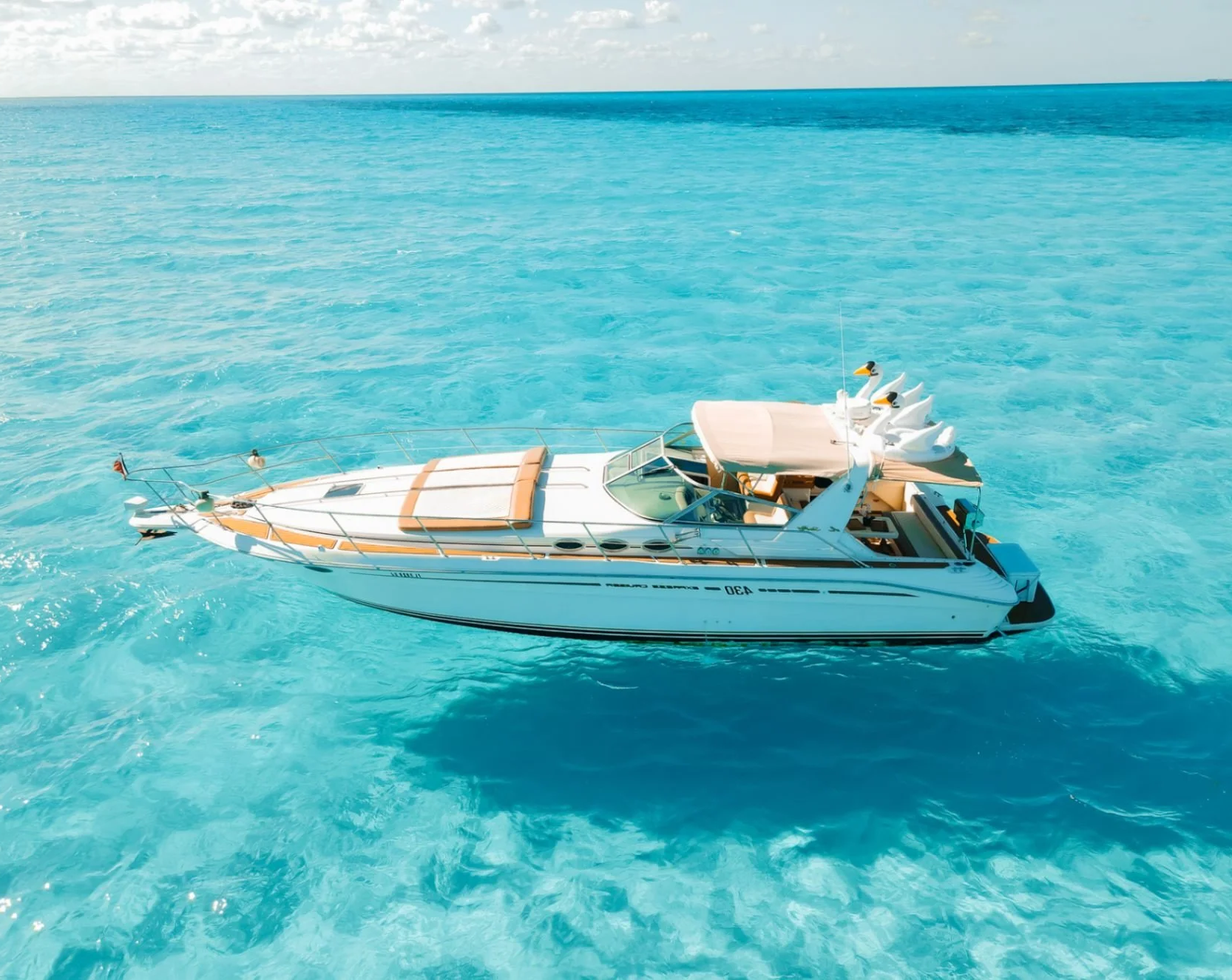 A luxury speedboat floating on clear blue ocean water under a partly cloudy sky.