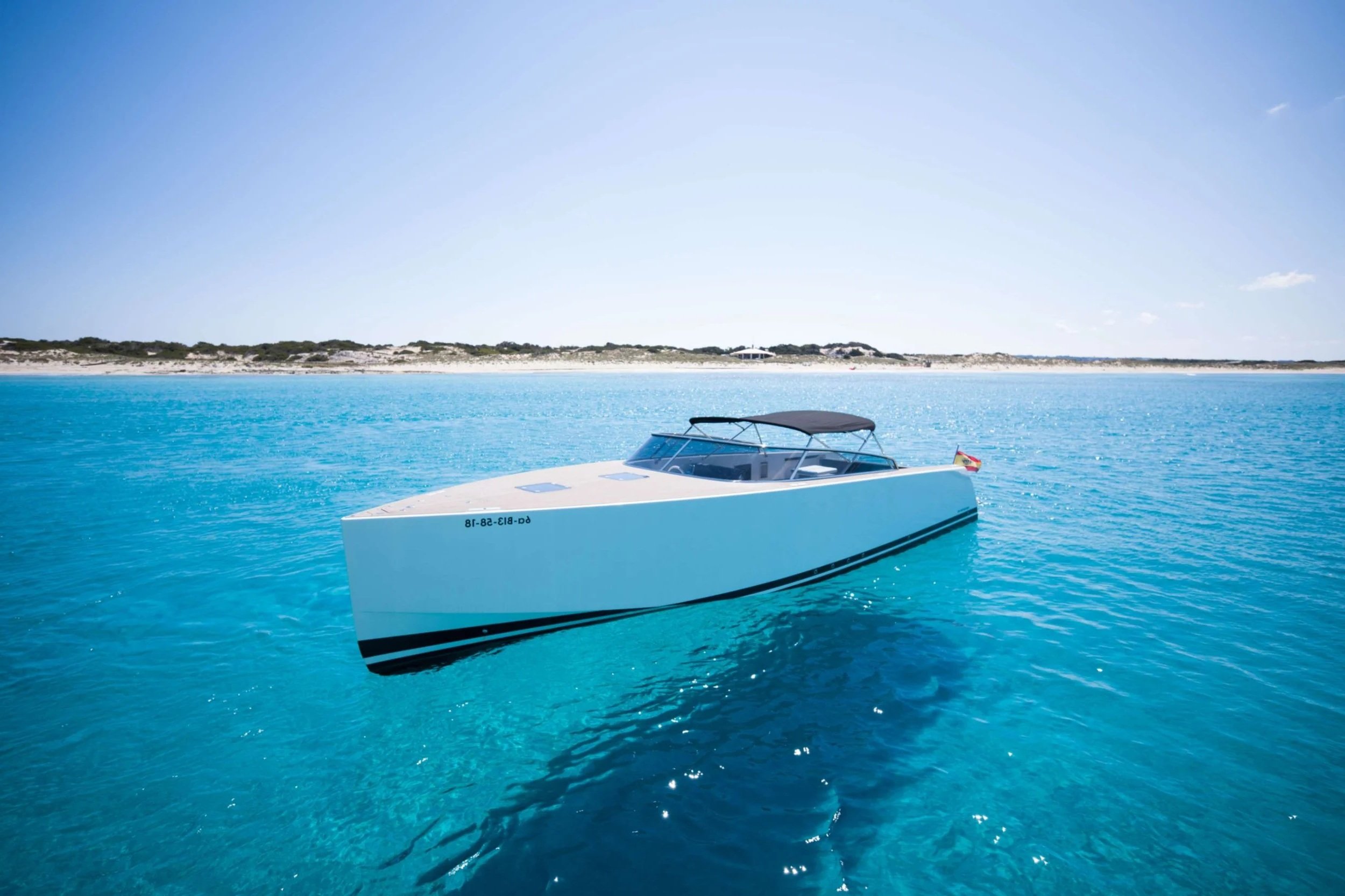 A white yacht floating on turquoise water near a sandy shoreline under a clear sky.