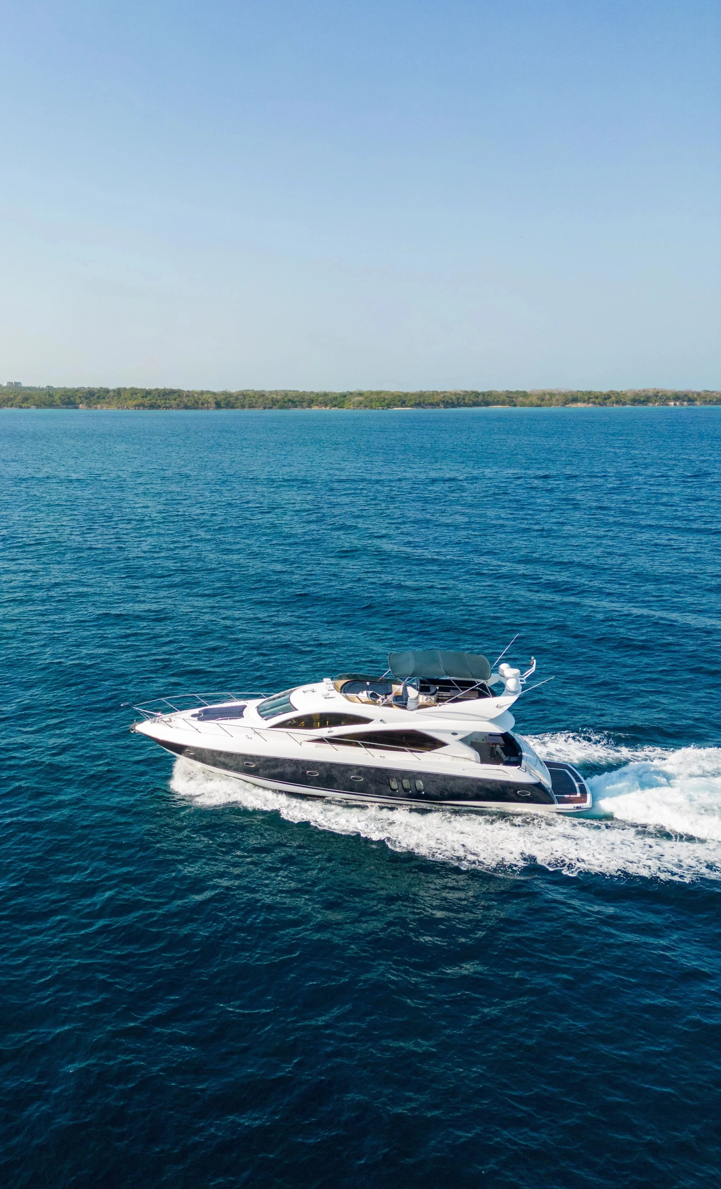 A white yacht cruising on blue ocean water with a distant shoreline and clear sky.