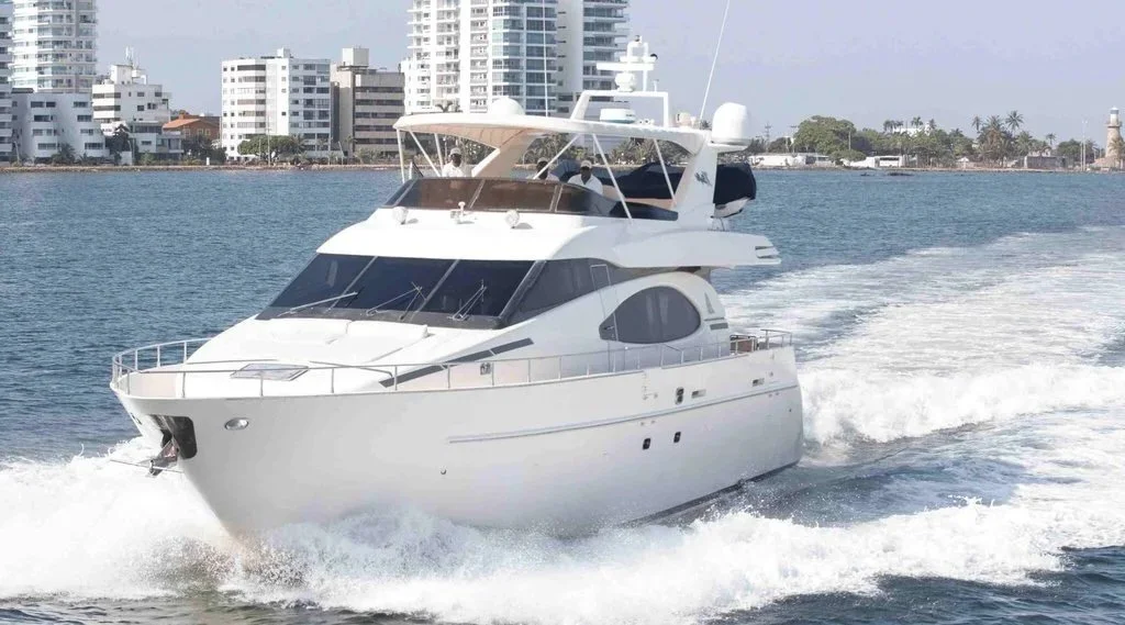 A white luxury motor yacht cruising on water near a city shoreline with modern buildings and palm trees in the background.