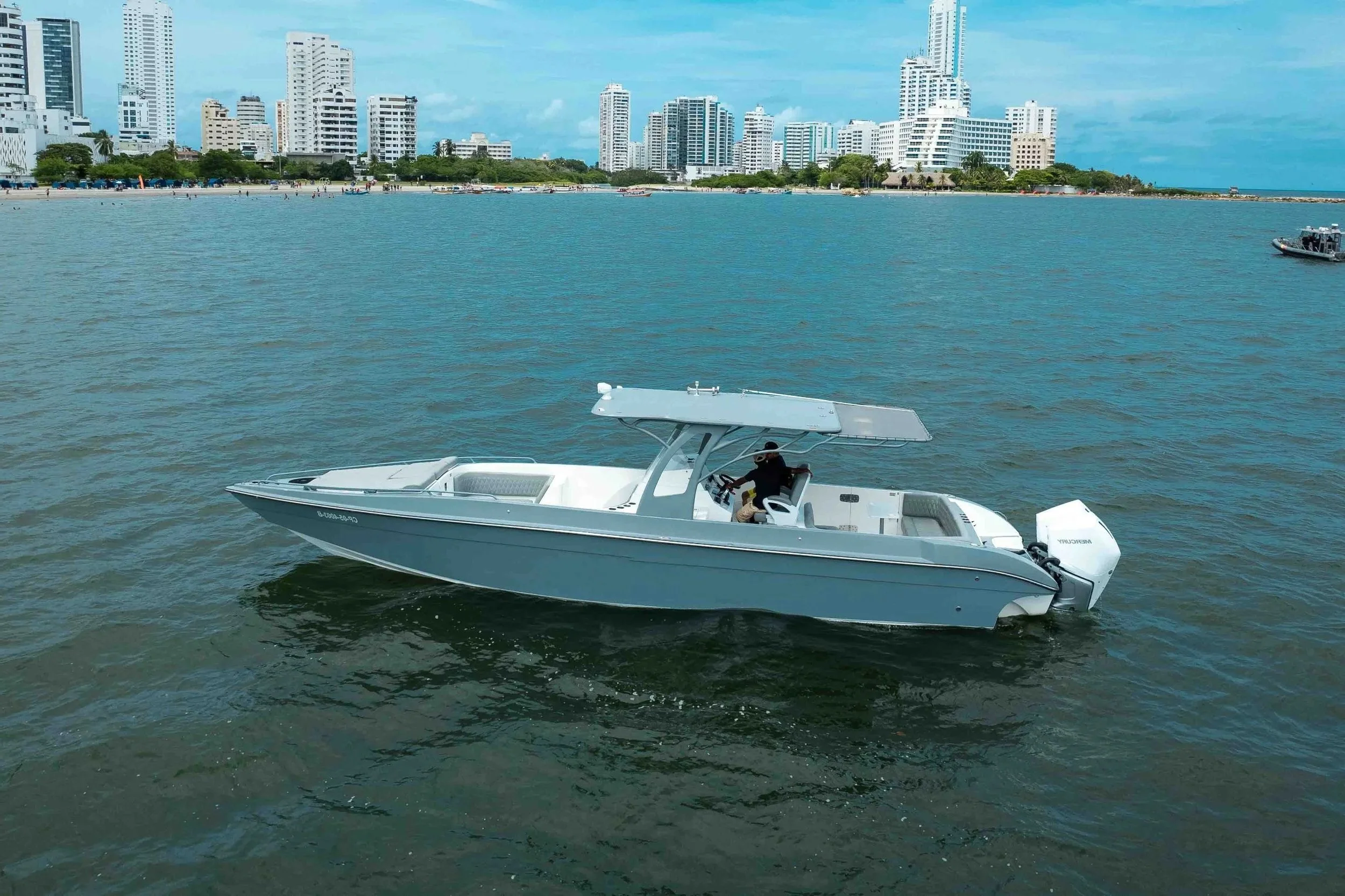 A white motorboat sailing in a body of water with a city skyline featuring tall modern buildings in the background.