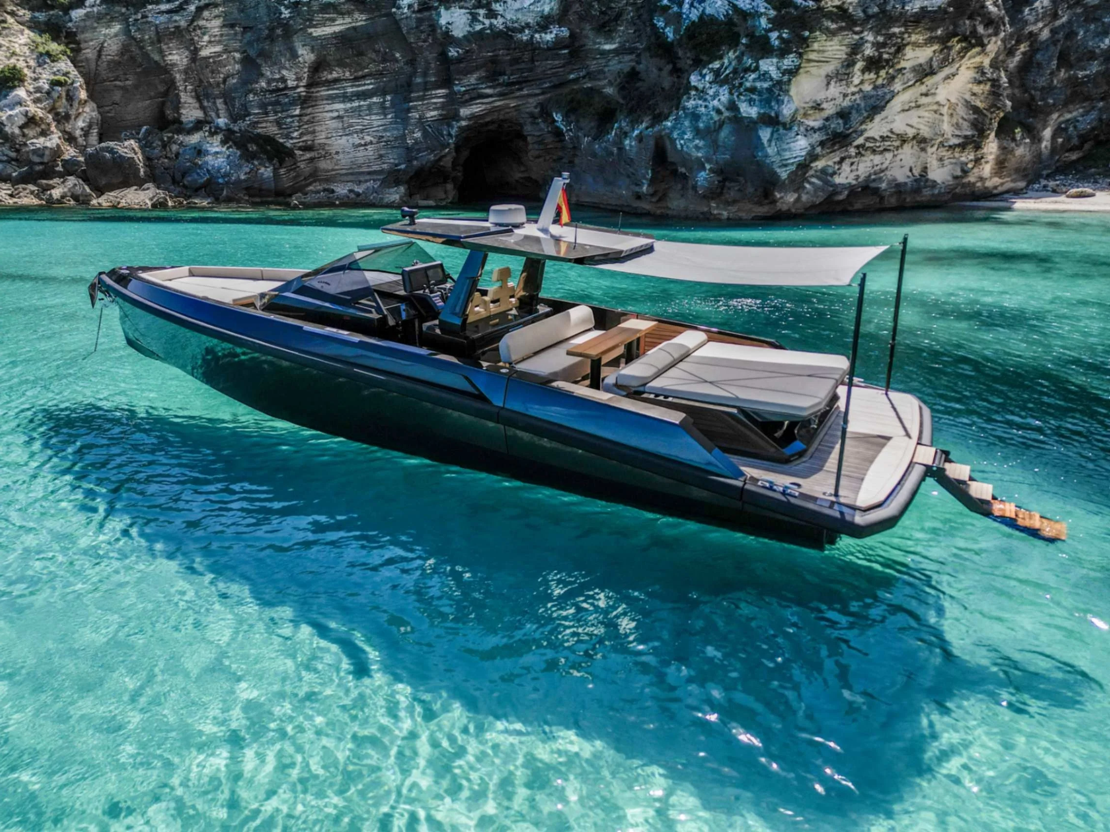 A modern luxury yacht floating on clear turquoise water near rocky cliffs.