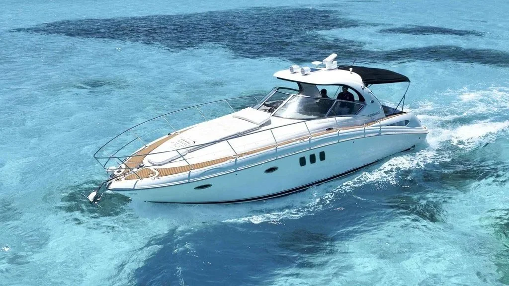 A white yacht with a black sunshade driving through clear blue water.