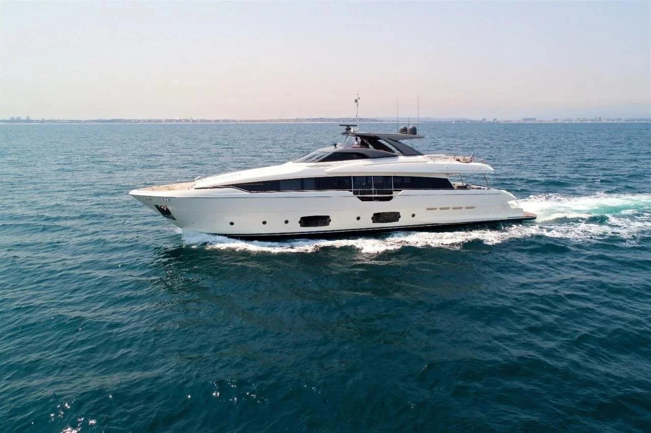 A luxury white yacht sailing on the open ocean with a distant shoreline on the horizon.