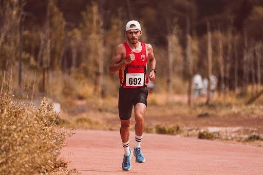 An athletic man wearing a tank top running on an outdoor road during a marathon race