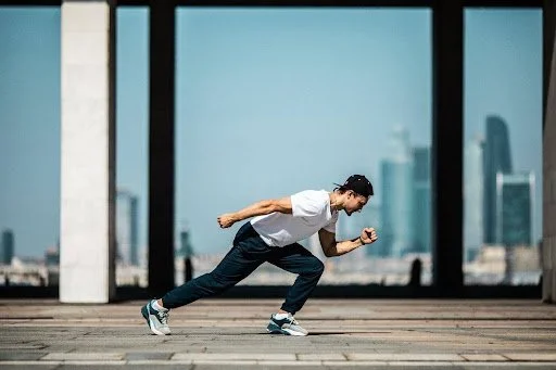 A man in a white t-shirt sprinting outdoors in a city setting wearing the best running shoes for heavy men