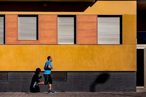 A man in a blue shirt jogging on a sunny city street showing the effort heavier runners put on their running shoes.
