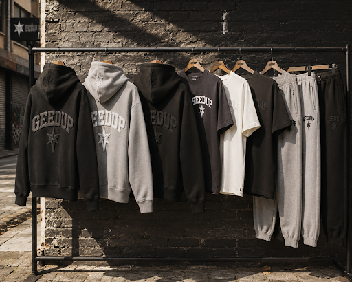 Folded Geedup Play For Keeps black hoodie stacked beside a Core PFK grey tracksuit on a wooden shelf.