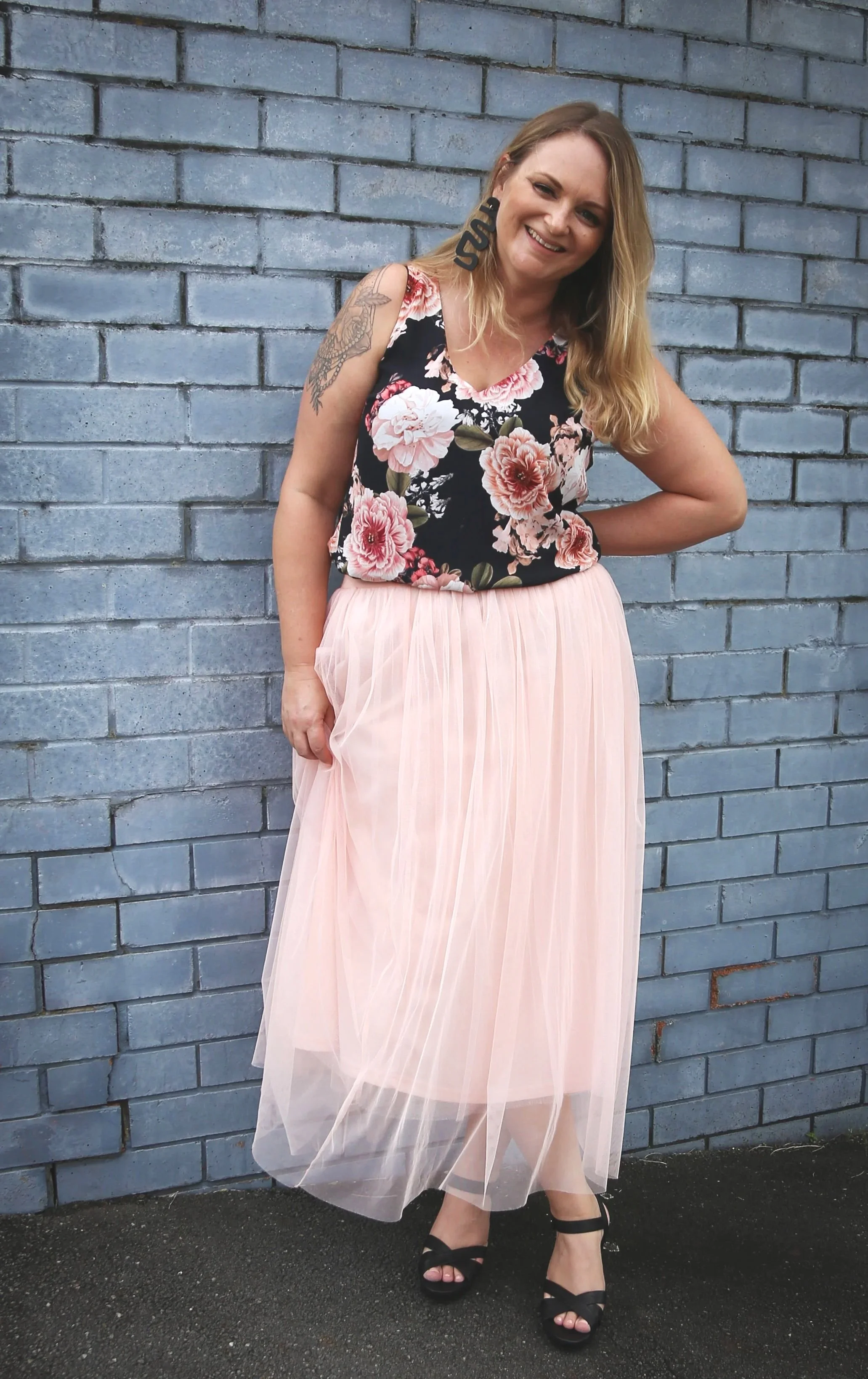 An image of Jade, head tilted, smiling warmly, wearing black floral top and pink tulle skirt.
