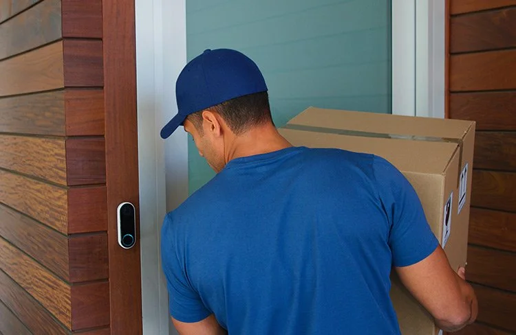 Delivery driver carrying a package to a Spartanburg home equipped with a smart video doorbell.